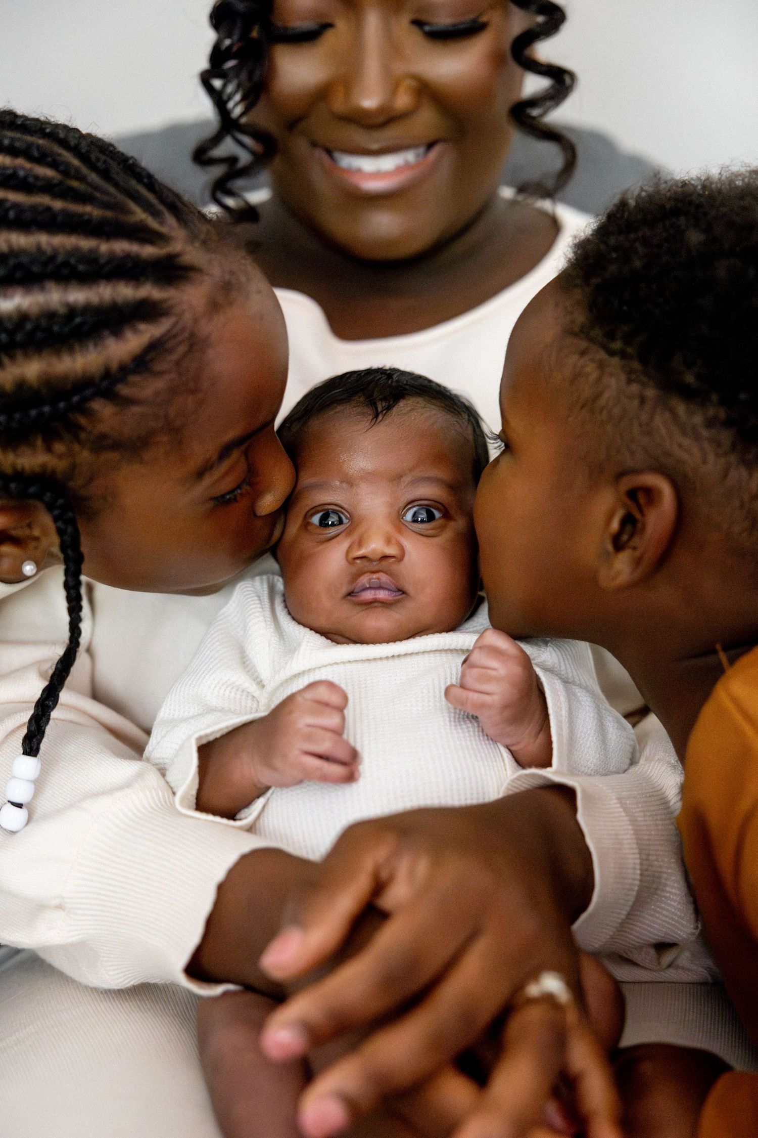 Family members in white and mustard clothing share loving interactions on bed.