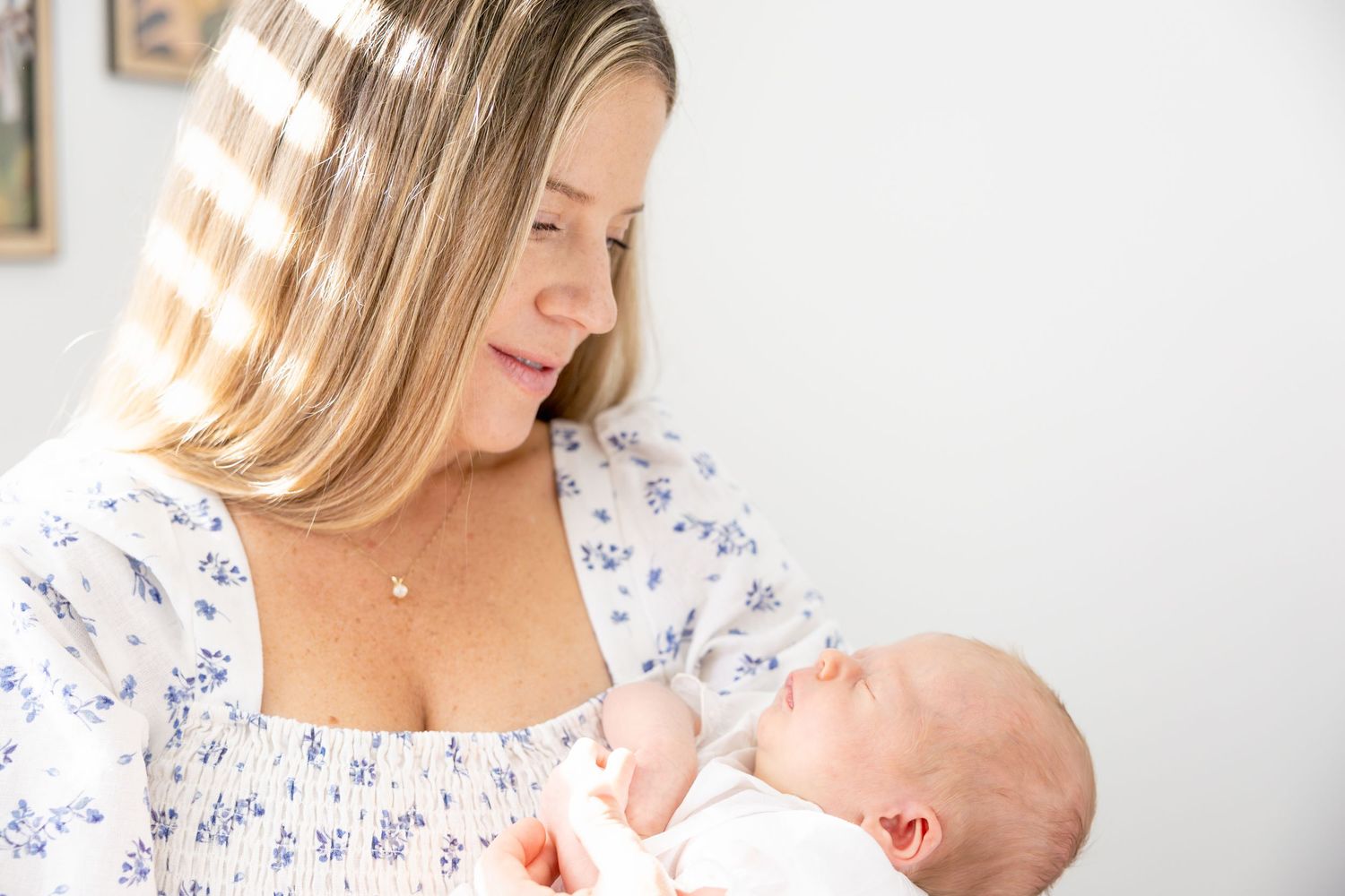 Mother gazes lovingly at newborn baby while holding them in floral dress.