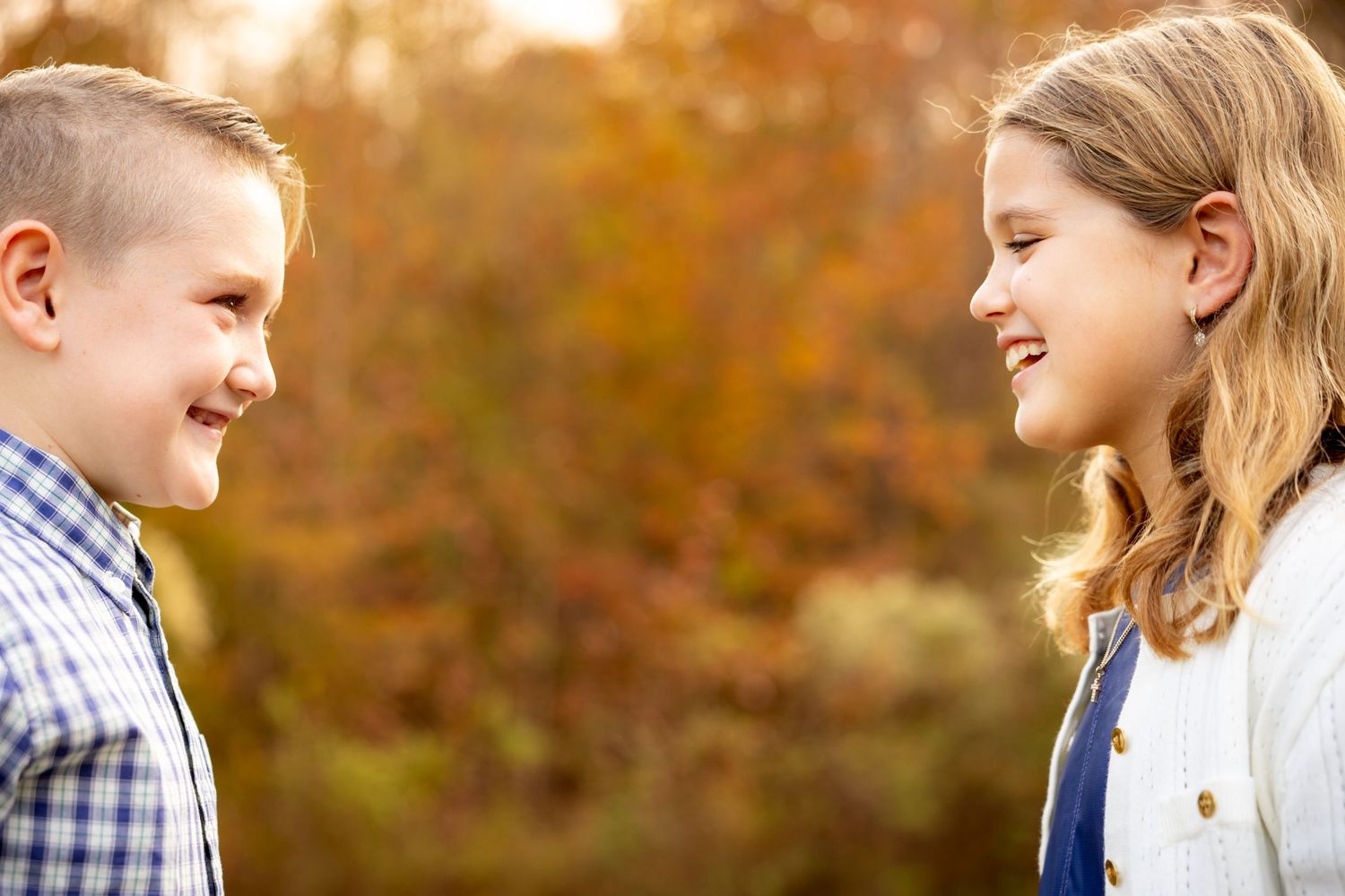 Two young people smiling at each other in a sunlit outdoor setting.