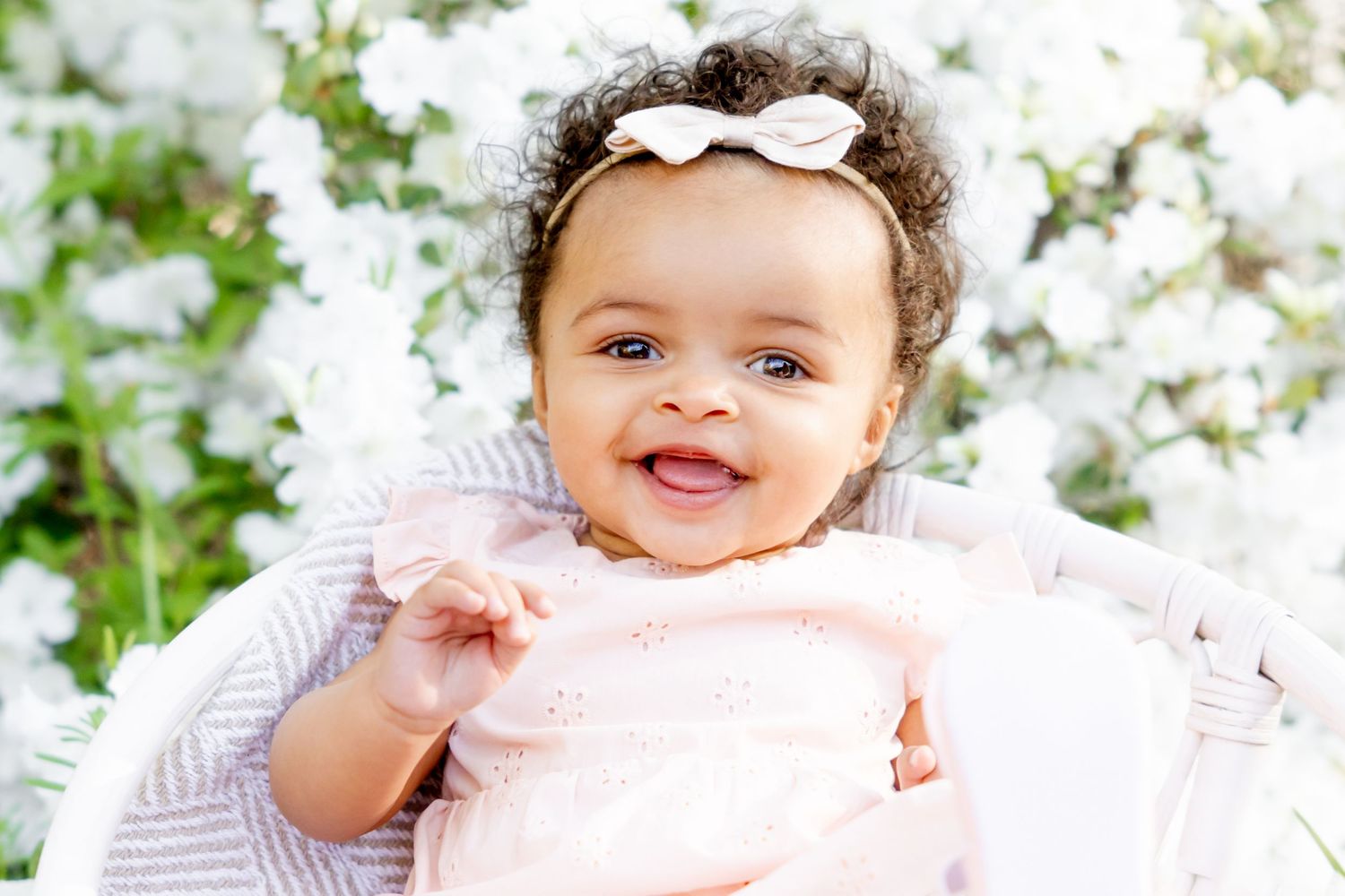 Baby in pink outfit smiling among white spring blossoms outdoors at Glencairn Gardens in Rock Hill, SC.
