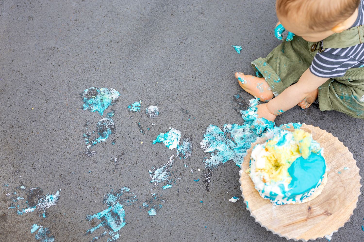 Overhead view of scattered blue cake crumbs and frosting on concrete during a cake smash.
