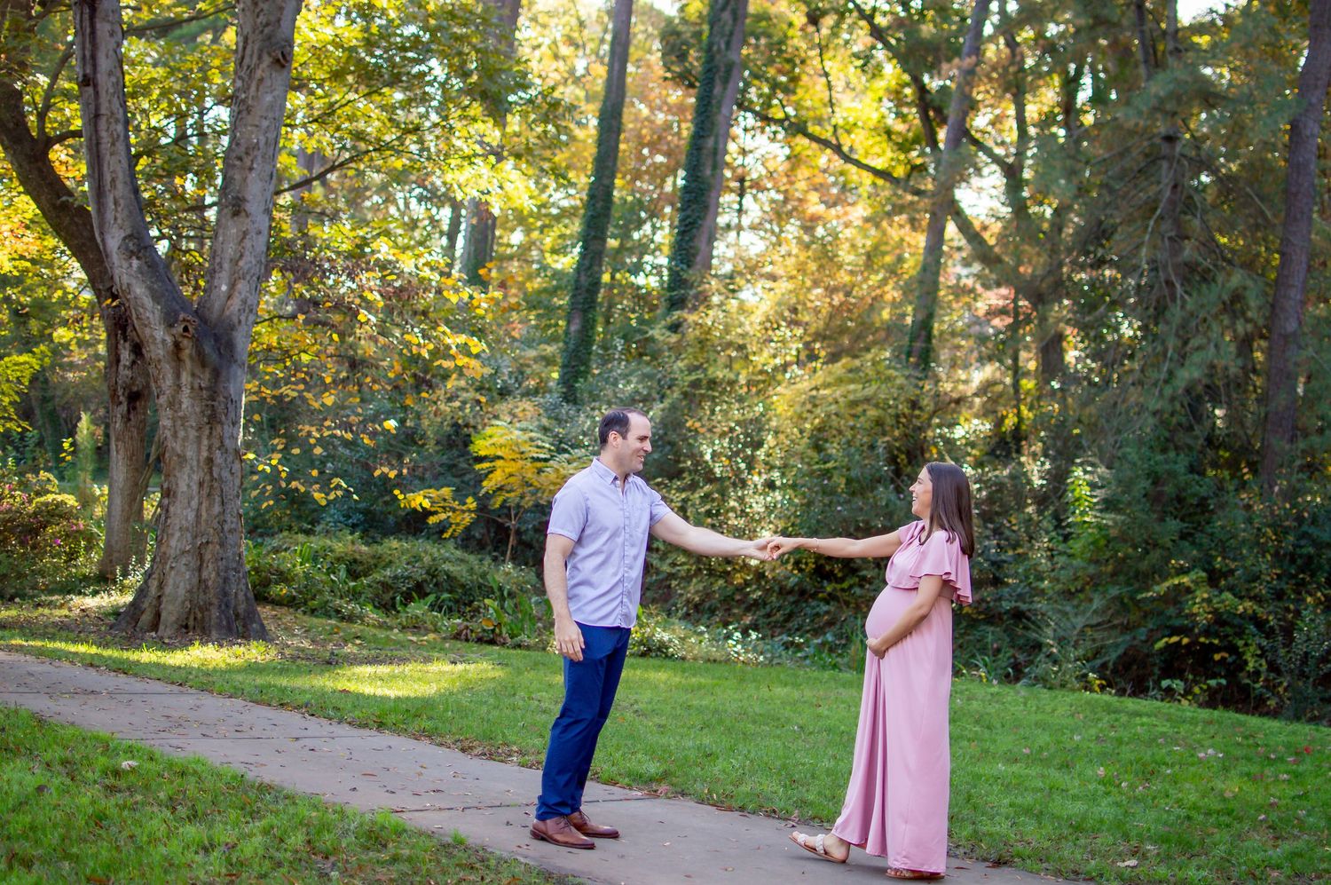 A couple shares a romantic moment in a lush garden setting during a maternity photoshoot.