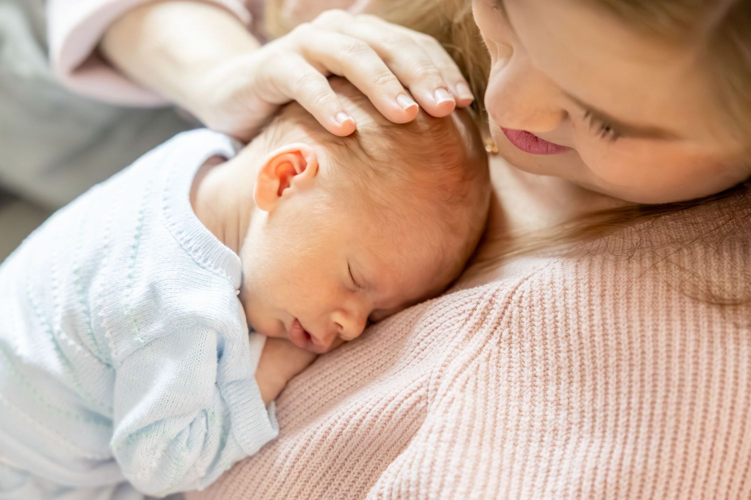 Tender moment of parent cradling sleeping newborn baby in soft pink and blue clothing.