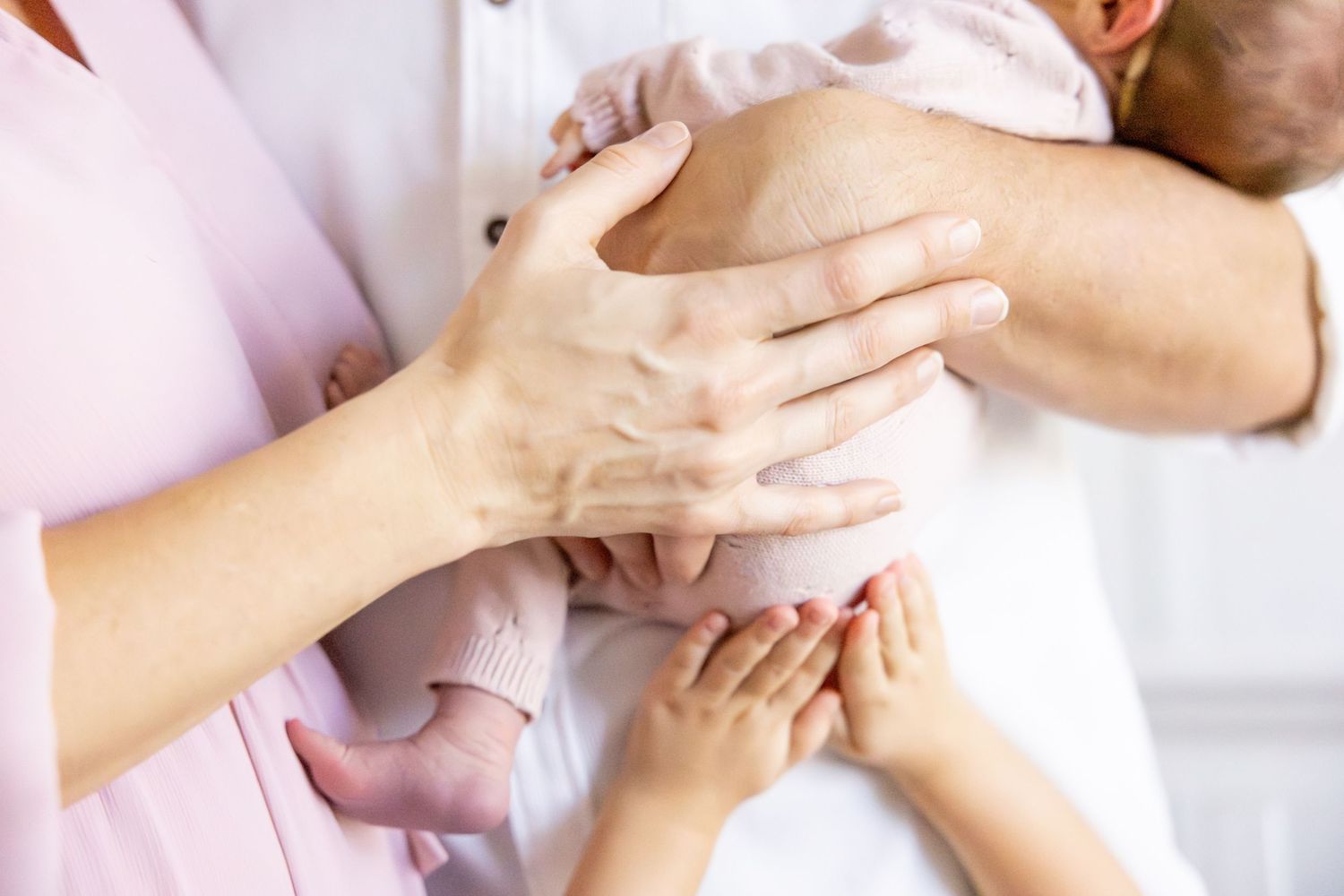 Close-up of gentle hands cradling a newborn baby wrapped in white.