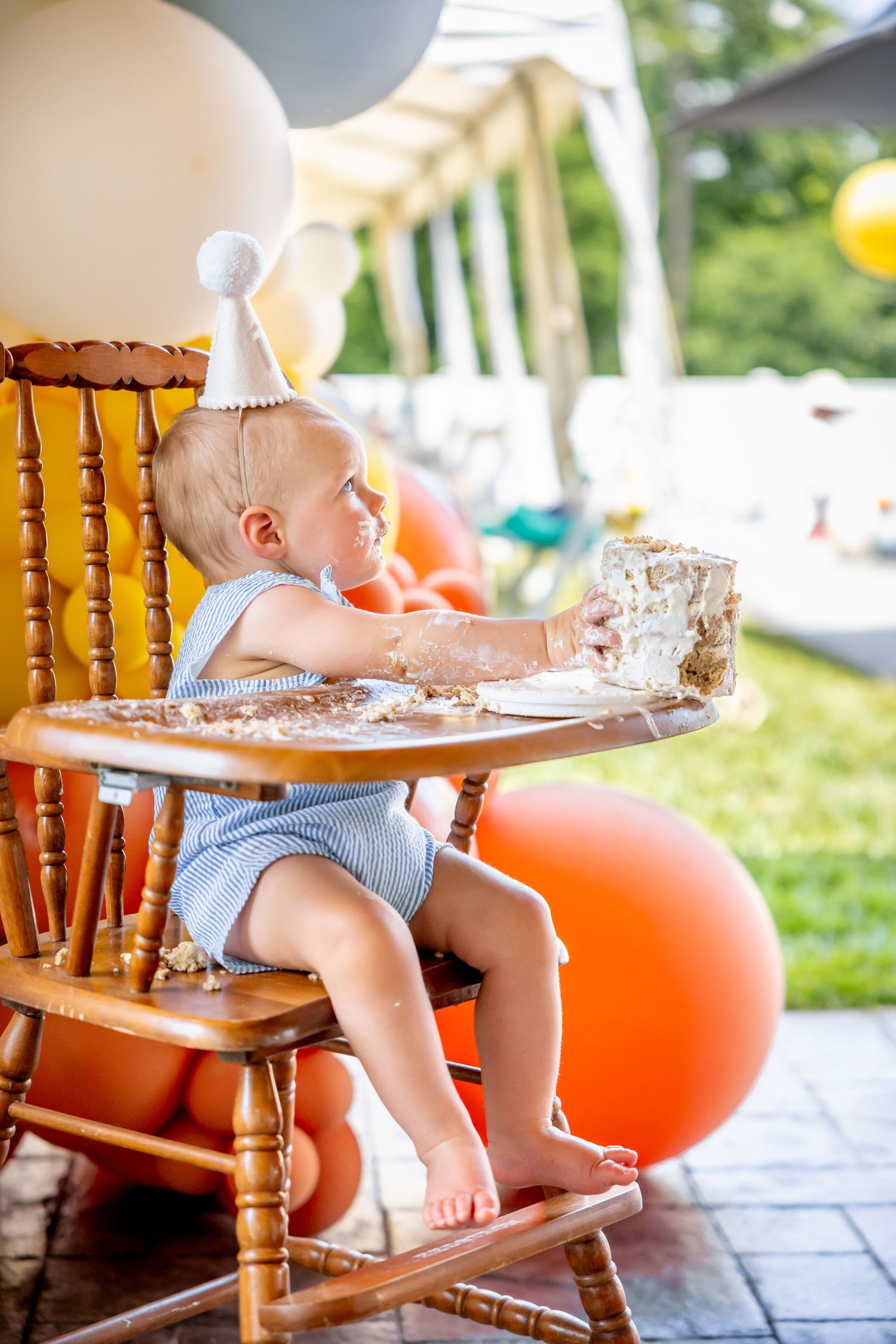Outdoor party setup with orange balloons and wooden chairs on stone patio.
