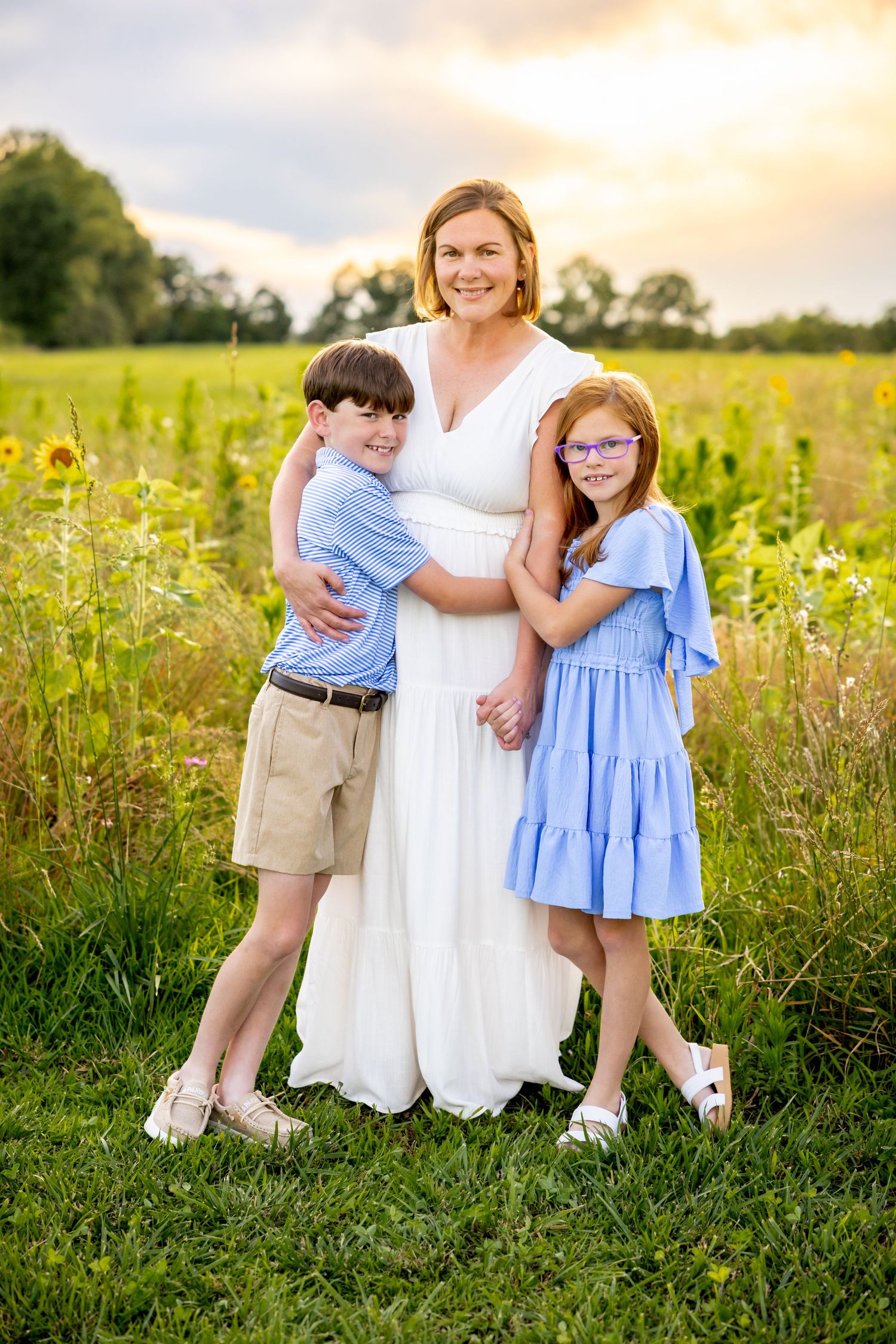 A joyful outdoor family portrait in a sunlit wildflower field showing sweet embraces and summer outfits at Blue Hill Garden in Monroe, NC.