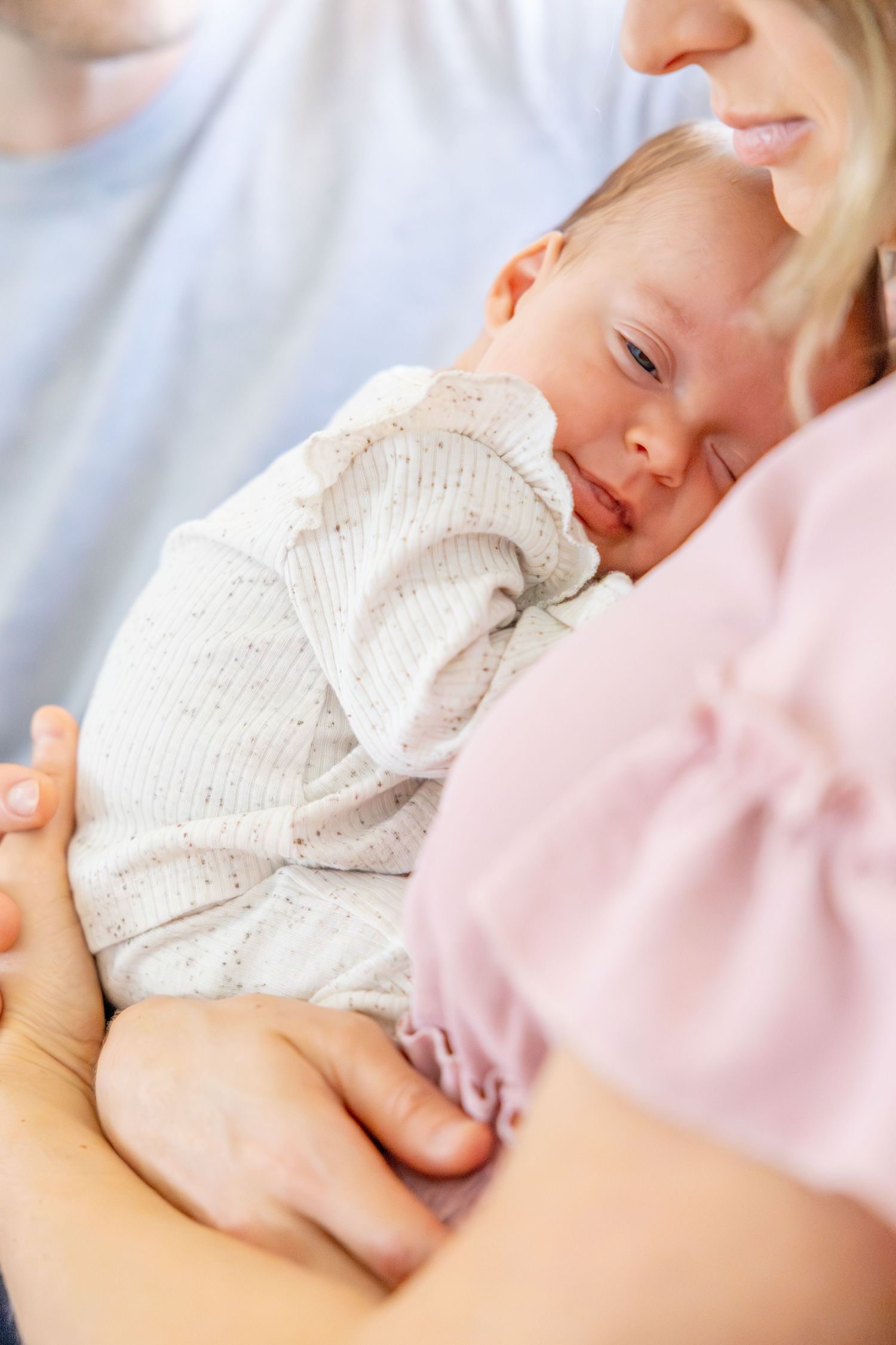 Sleeping newborn in white sweater nestled against pink clothing.