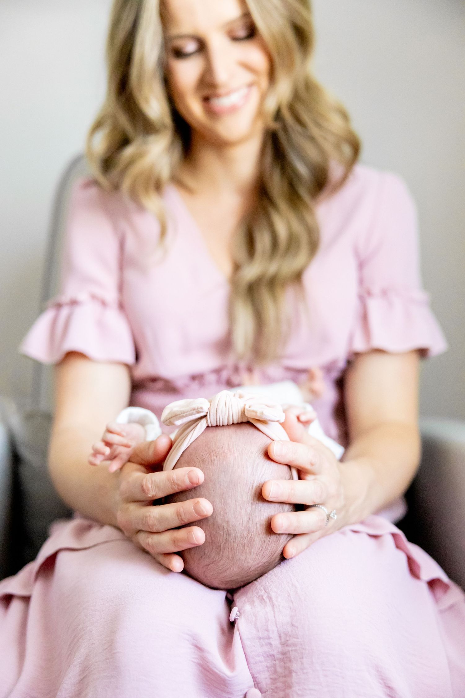 Woman in pink dress holding sleeping baby while sitting indoors.