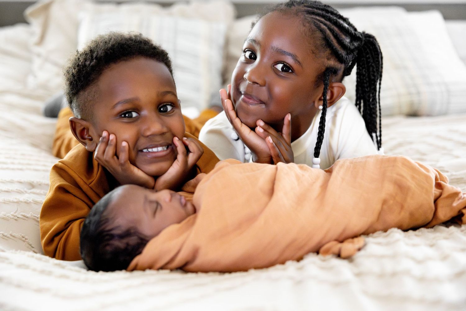 Children sharing happy expressions while lying on white bedding.