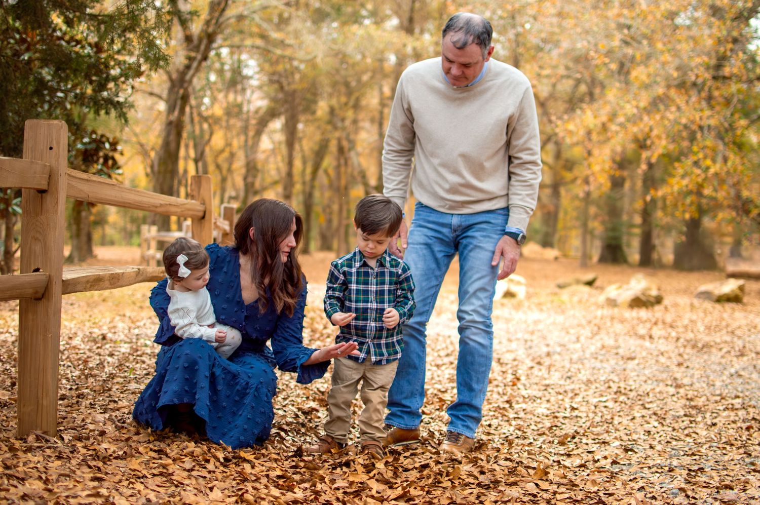 A family gathers together on a leaf-covered path in an autumn forest setting at Westminster Park in Rock Hill, SC.