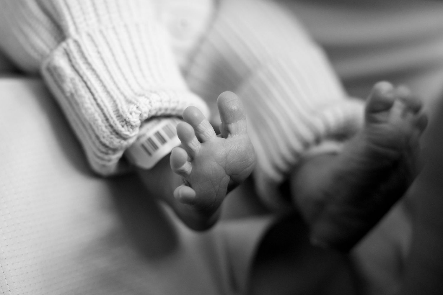 Black and white macro shot of tiny newborn feet in knit booties.
