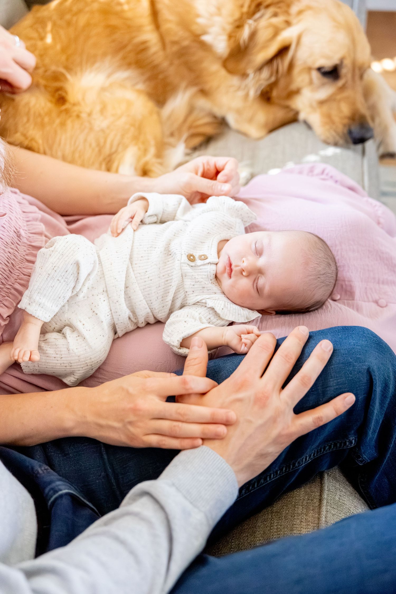 Sleeping newborn baby in white onesie rests peacefully with golden retriever nearby.