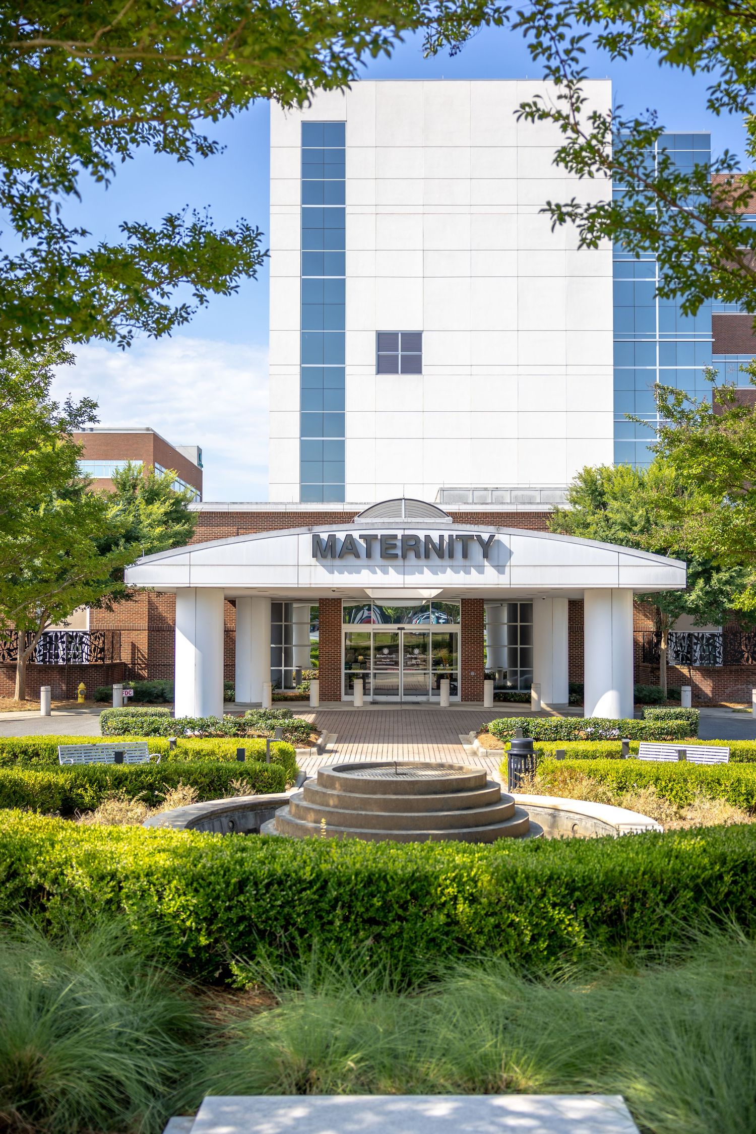 Modern maternity hospital entrance with landscaped garden and glass facade.