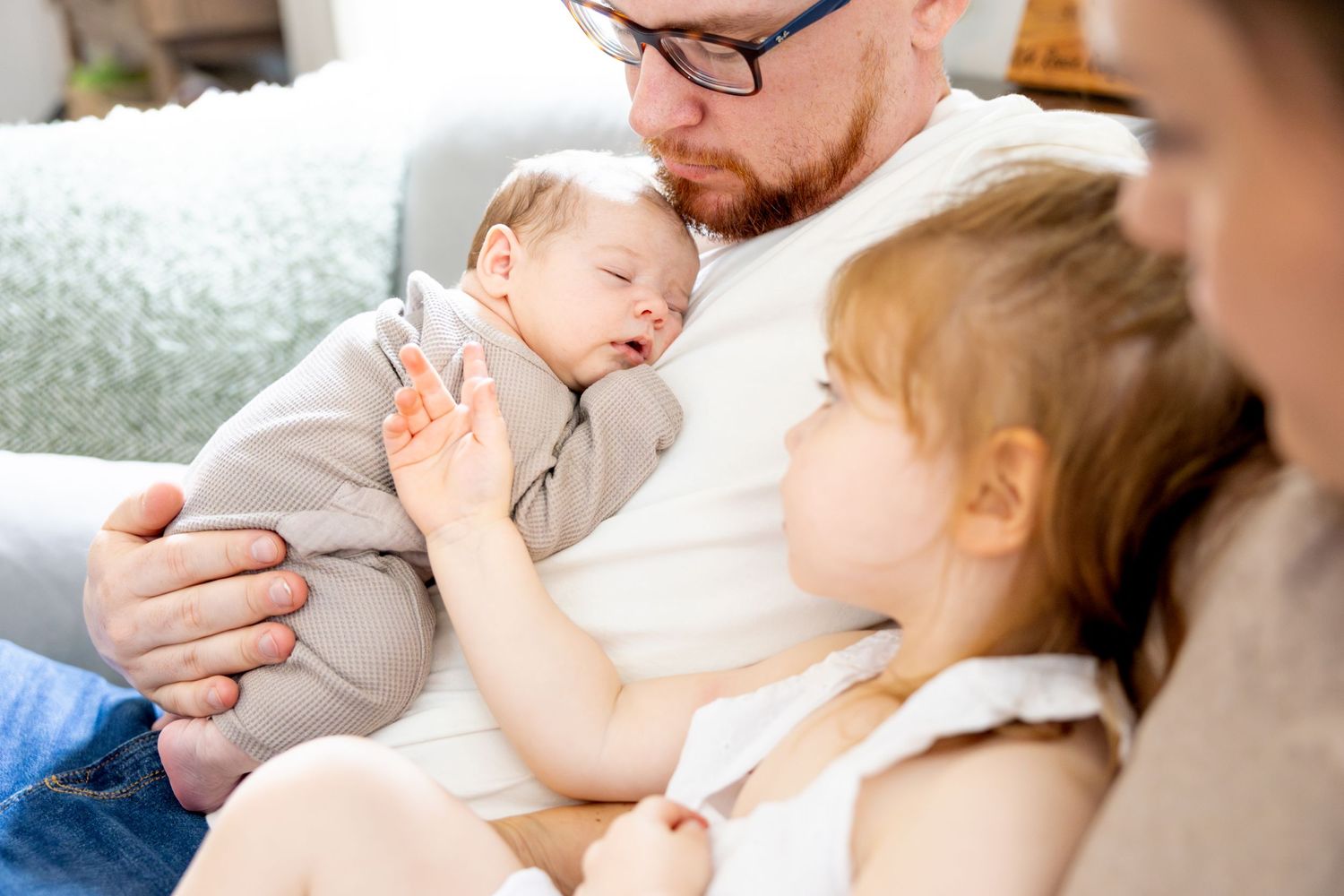 Family cuddles together on a couch while looking at their sleeping baby.