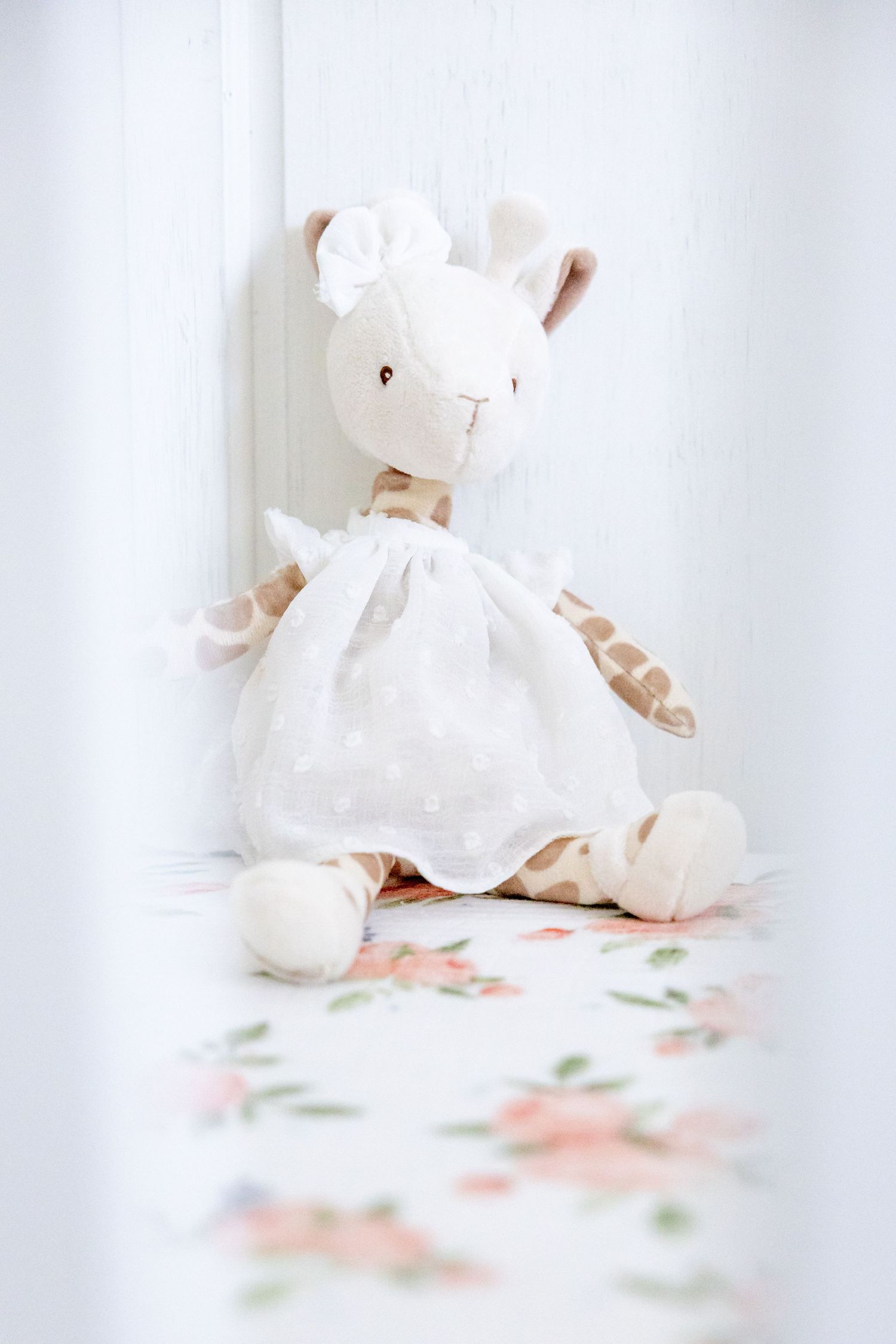 White stuffed bunny toy wearing dress sits on floral patterned surface.