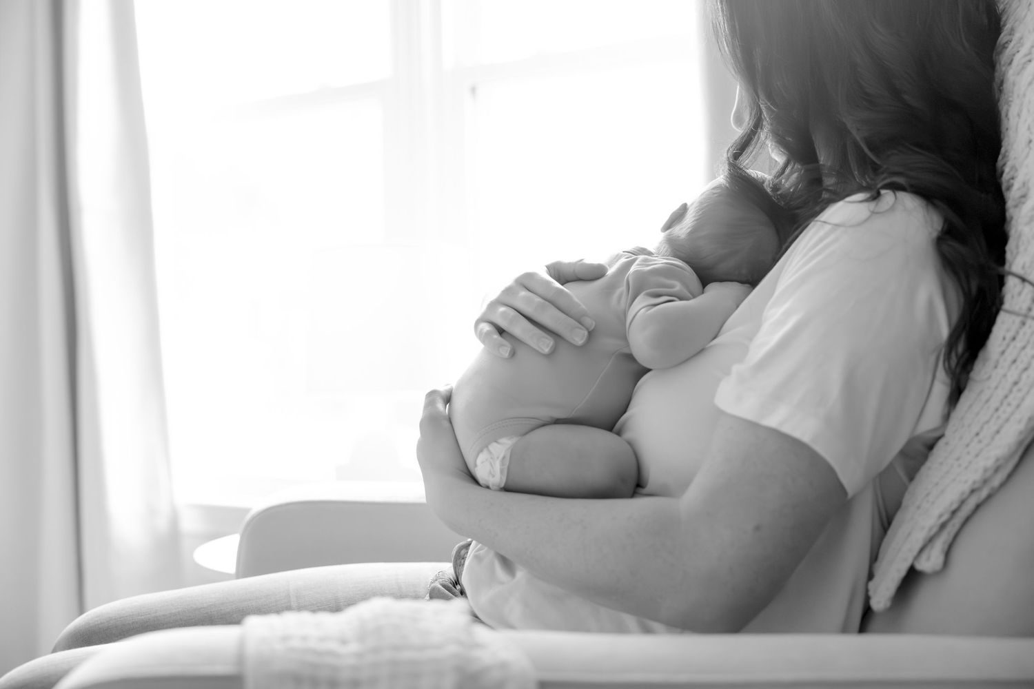 Silhouetted side view of parent holding sleeping infant near window in peaceful moment.