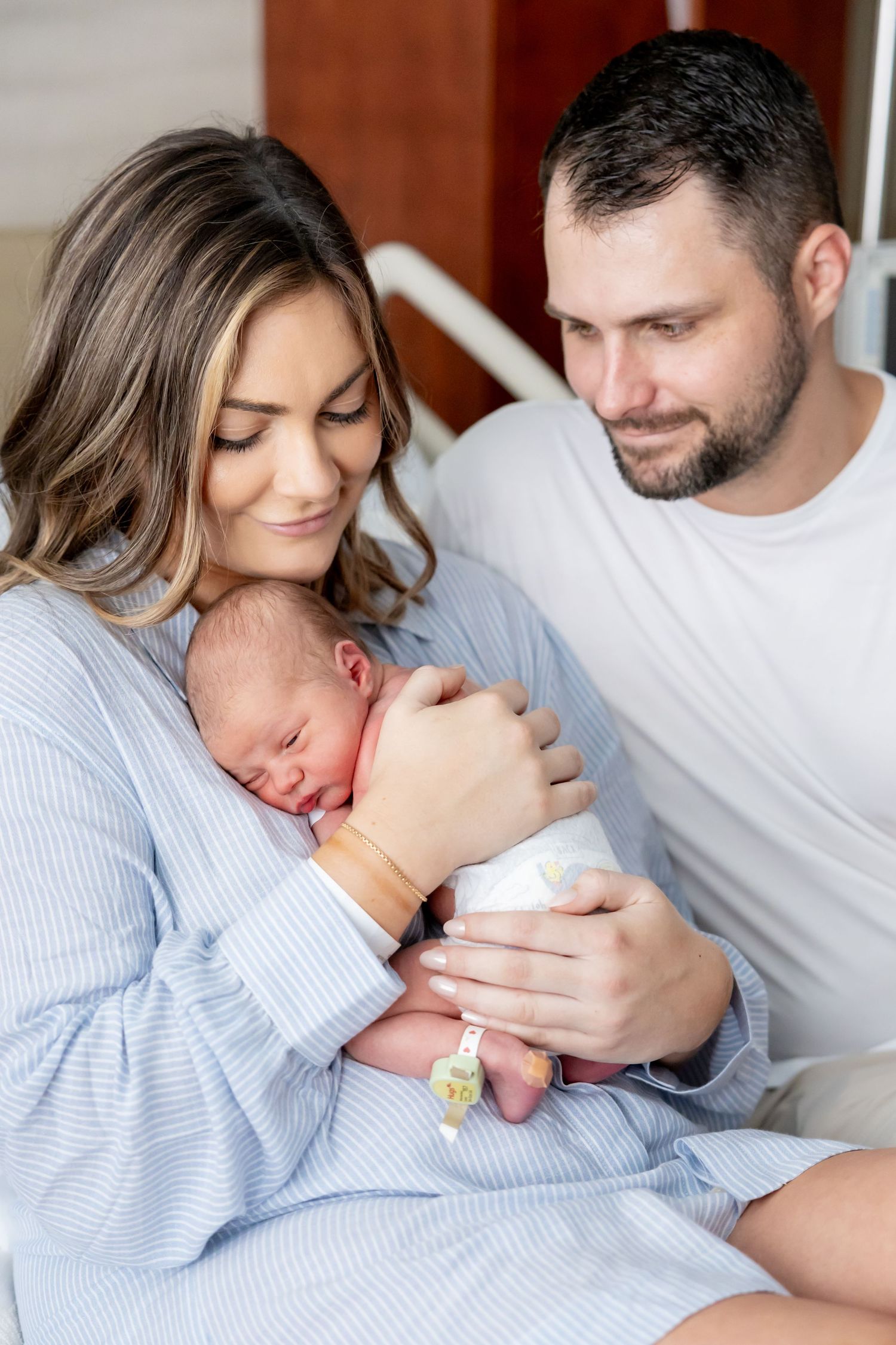 New parents sharing tender moment with sleeping newborn in hospital room.