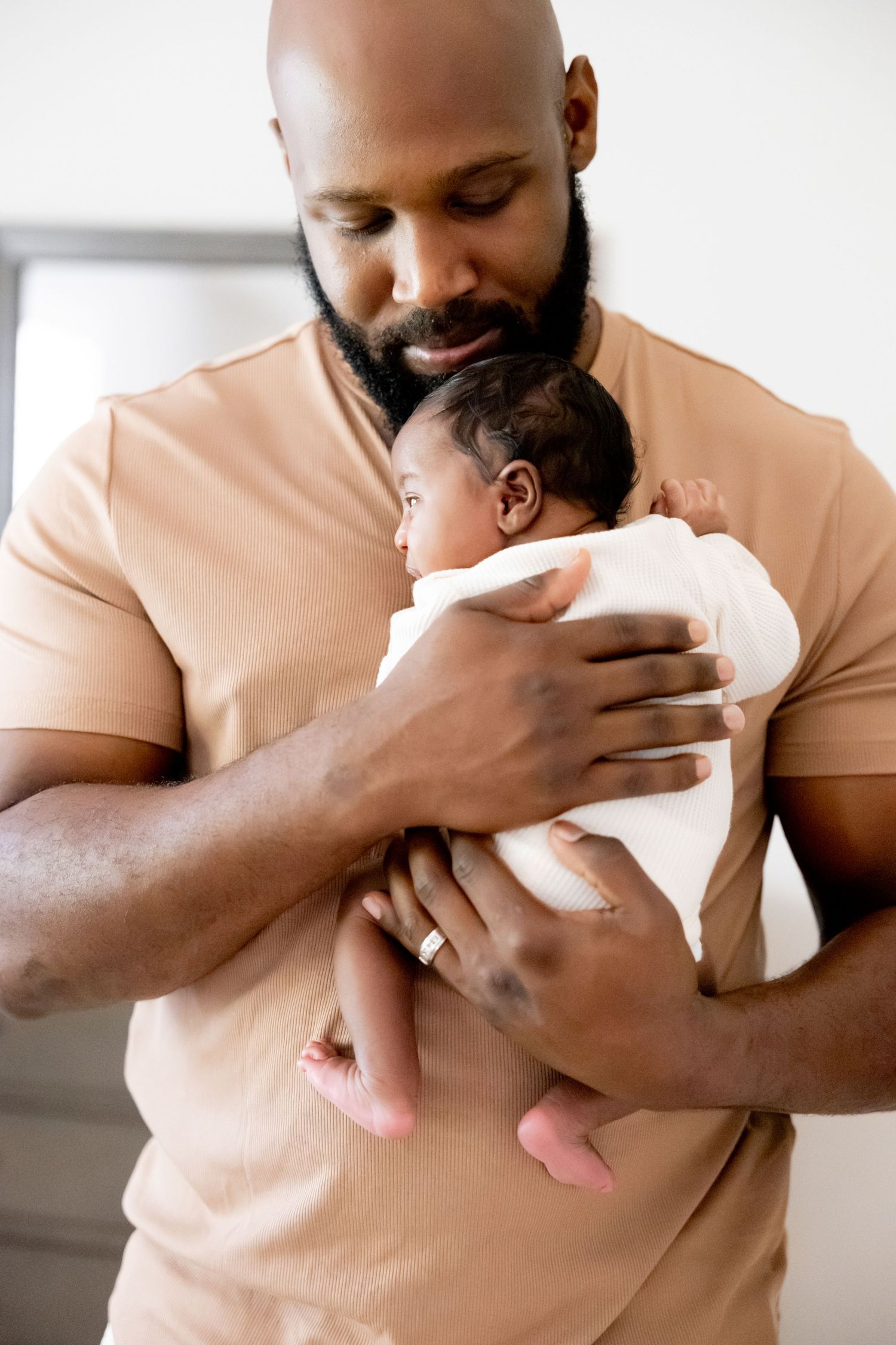 Tender moment showing arms holding sleeping newborn wrapped in white.