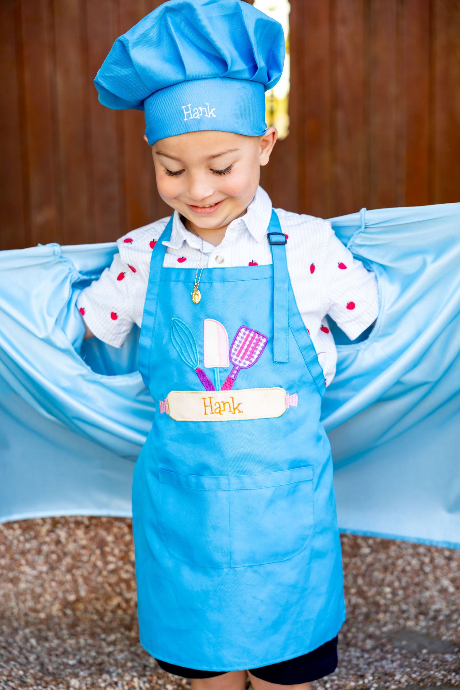 A young preschool graduate showing off his chef attire in a light blue chef's hat and apron.
