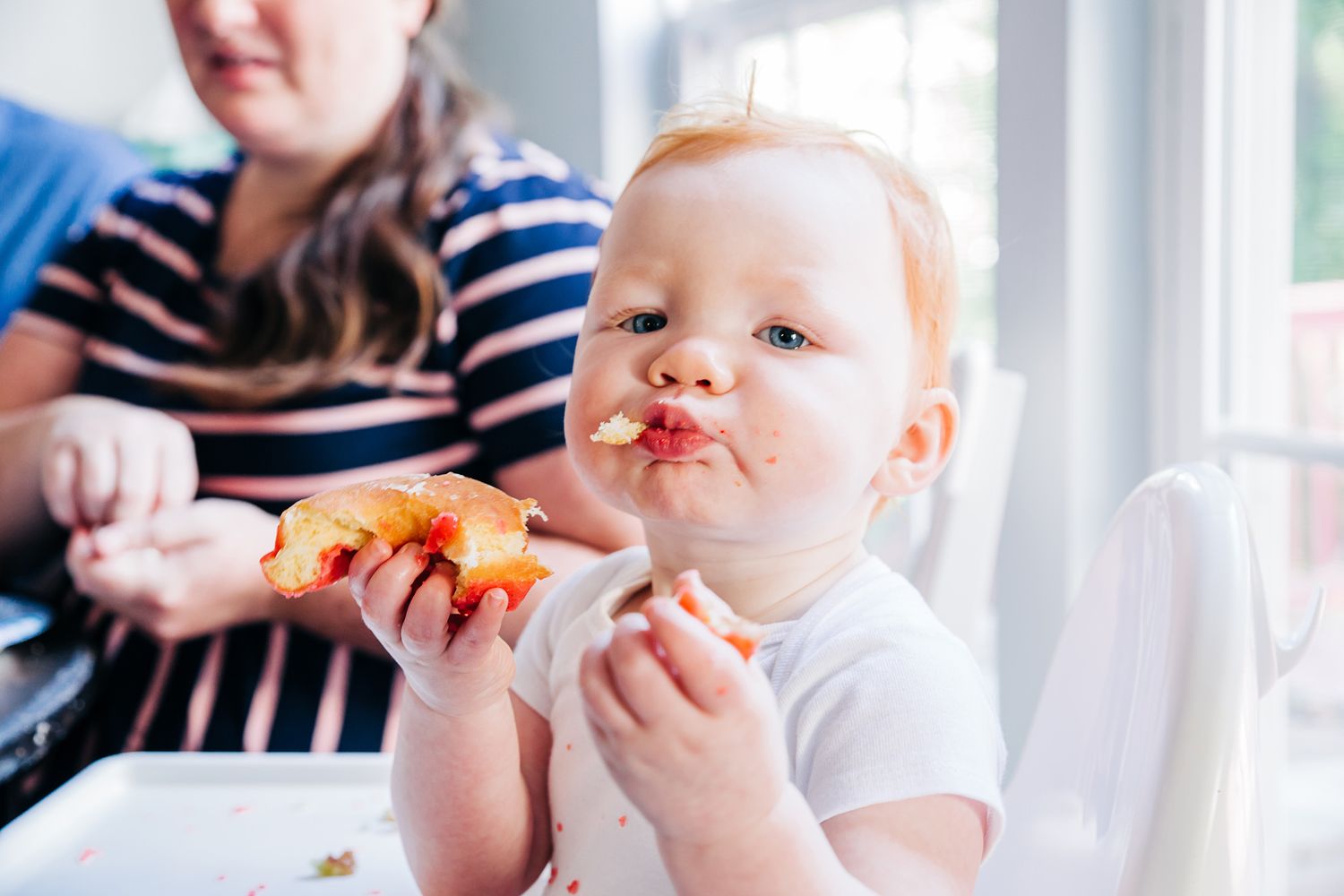 Baby eating food in natural window light during mealtime.