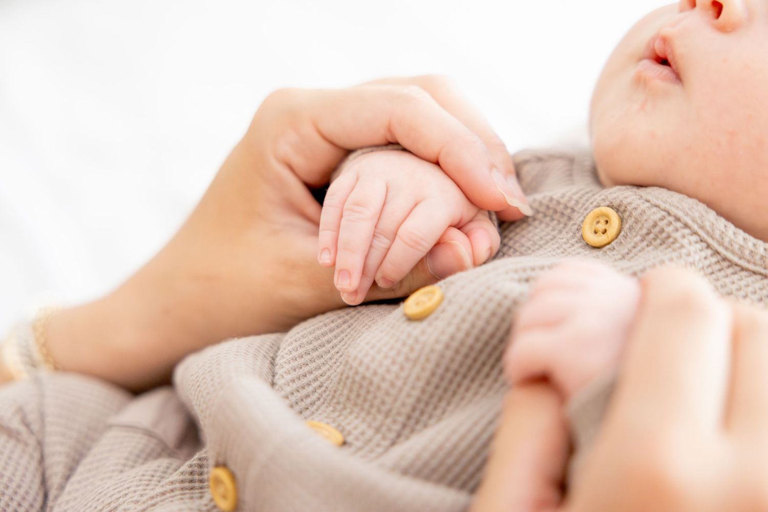 Close up of adult hands holding tiny baby hand on gray knit fabric.