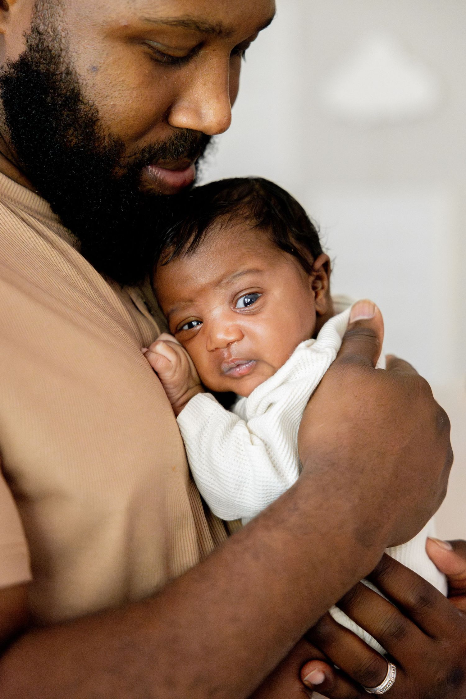 A tender moment shows a gentle embrace with a young baby being held lovingly against a soft beige background.