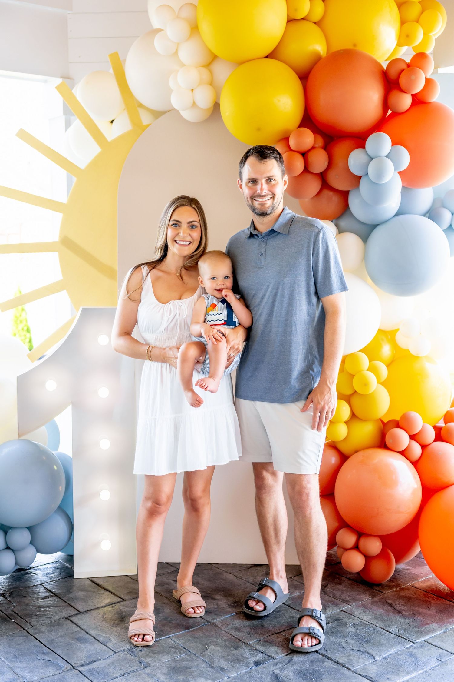 Family portrait against wall decorated with colorful balloon arch in orange, yellow and blue.