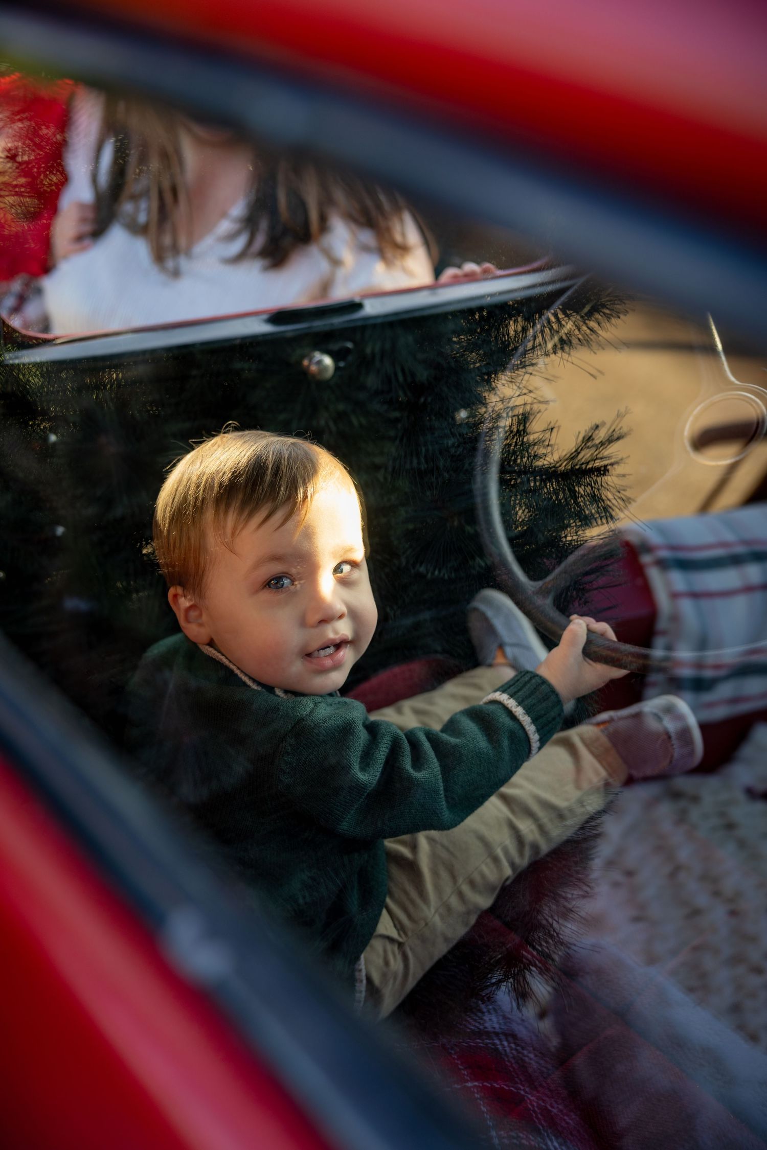 View through a car window showing someone inside a red vehicle.