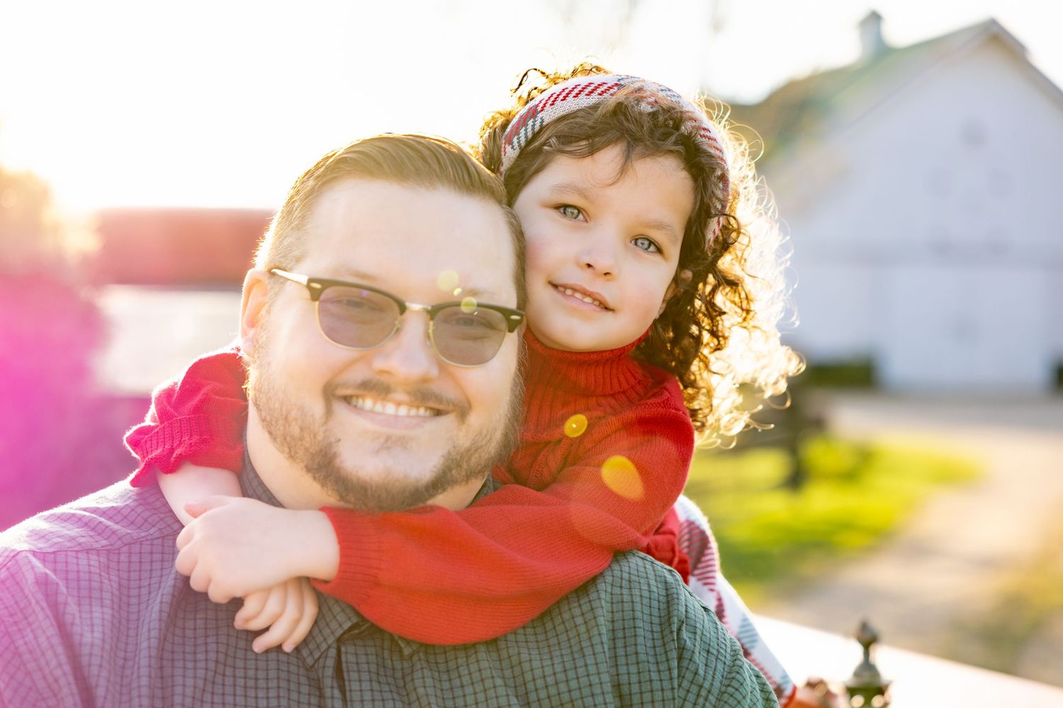 Warm sunset portrait showing playful piggyback ride against rustic farm backdrop.