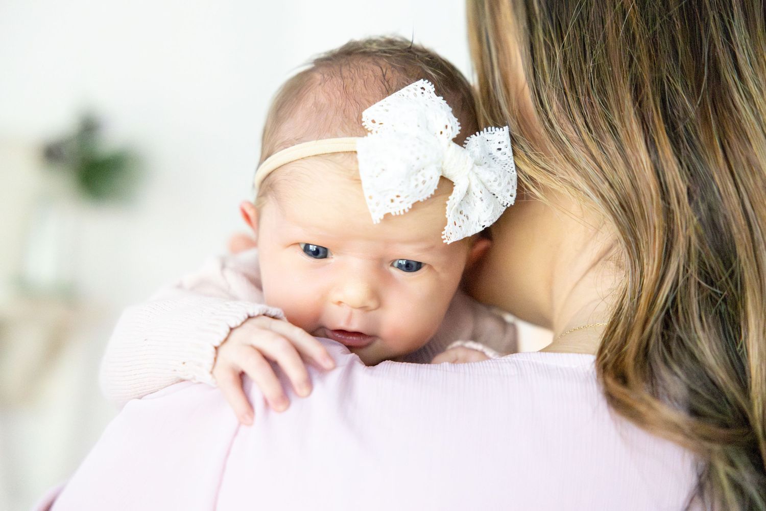 Parents in white and pink clothing cuddle their newborn baby in an intimate home portrait.