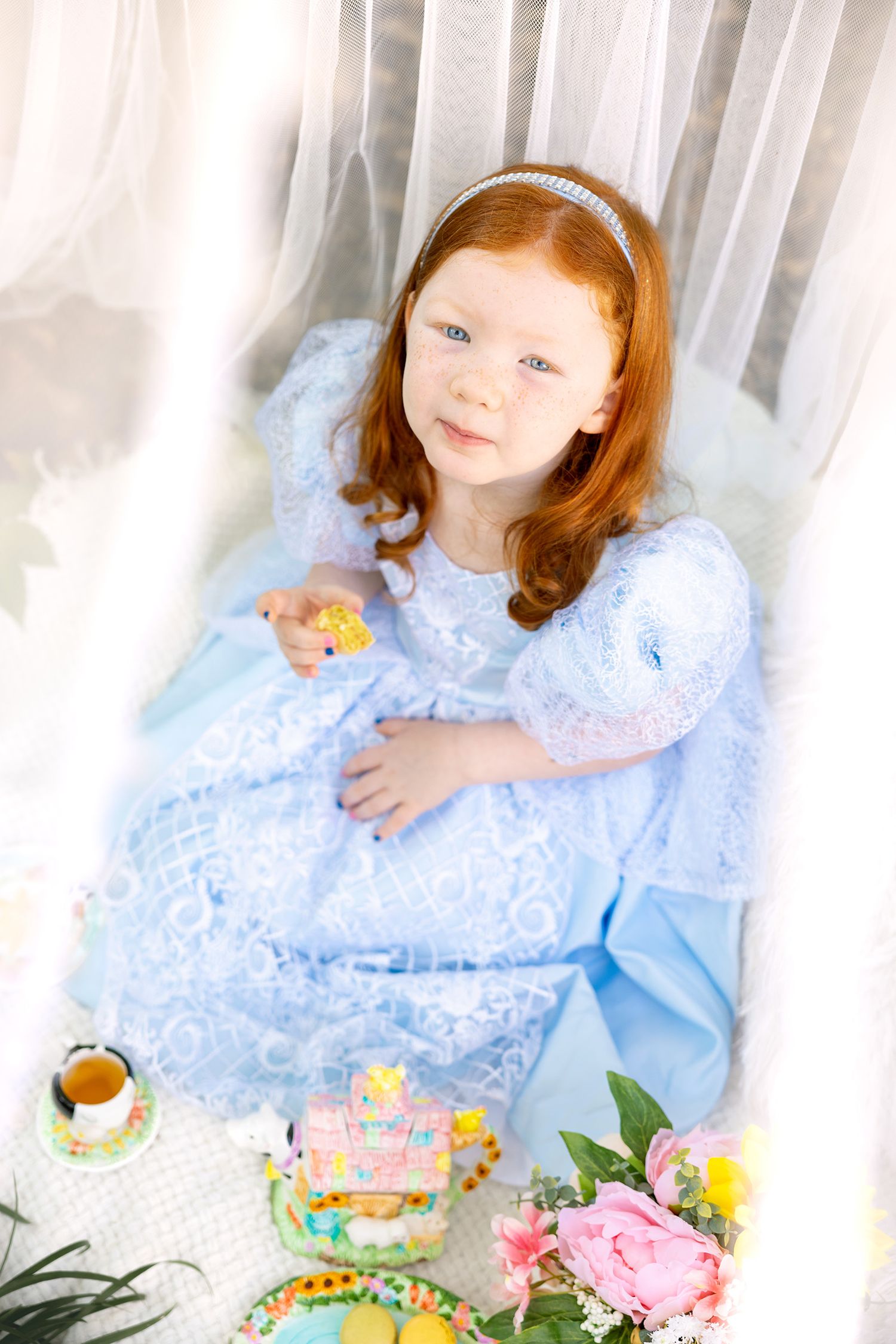 Child in blue lace dress poses with floral decorations and spring tea party setting.
