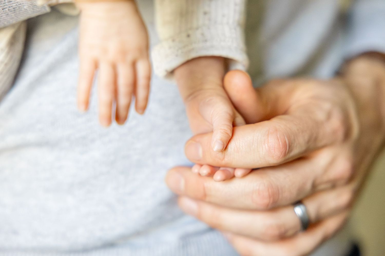 Close-up of gentle hands holding delicate newborn details against grey fabric background.
