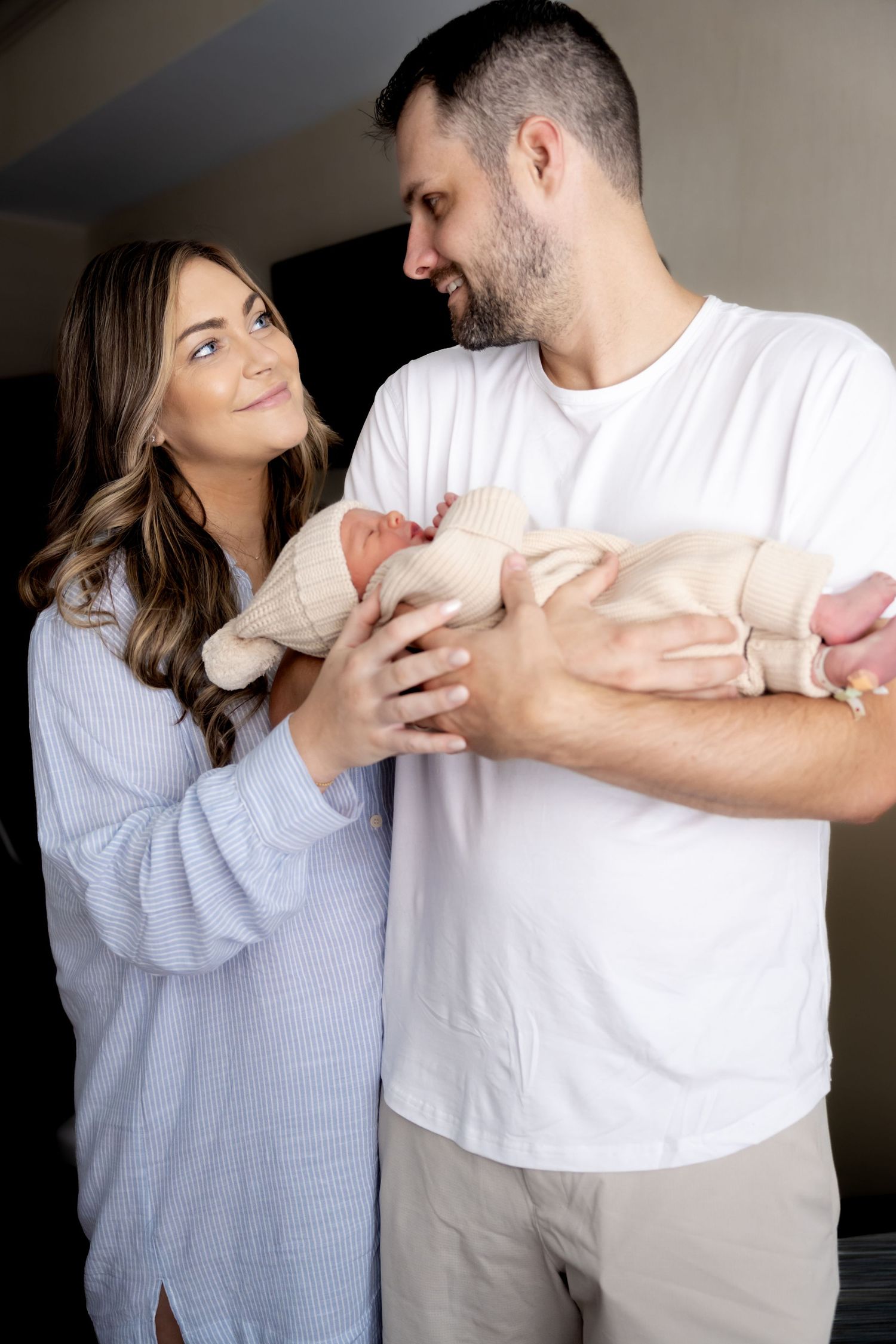 Couple tenderly holds their newborn baby swaddled in soft beige knit fabric.