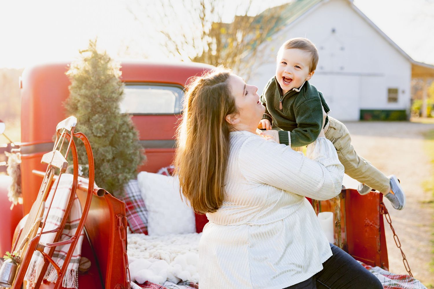 Joyful winter scene with parent and child playing in back of vintage red truck with Christmas tree.