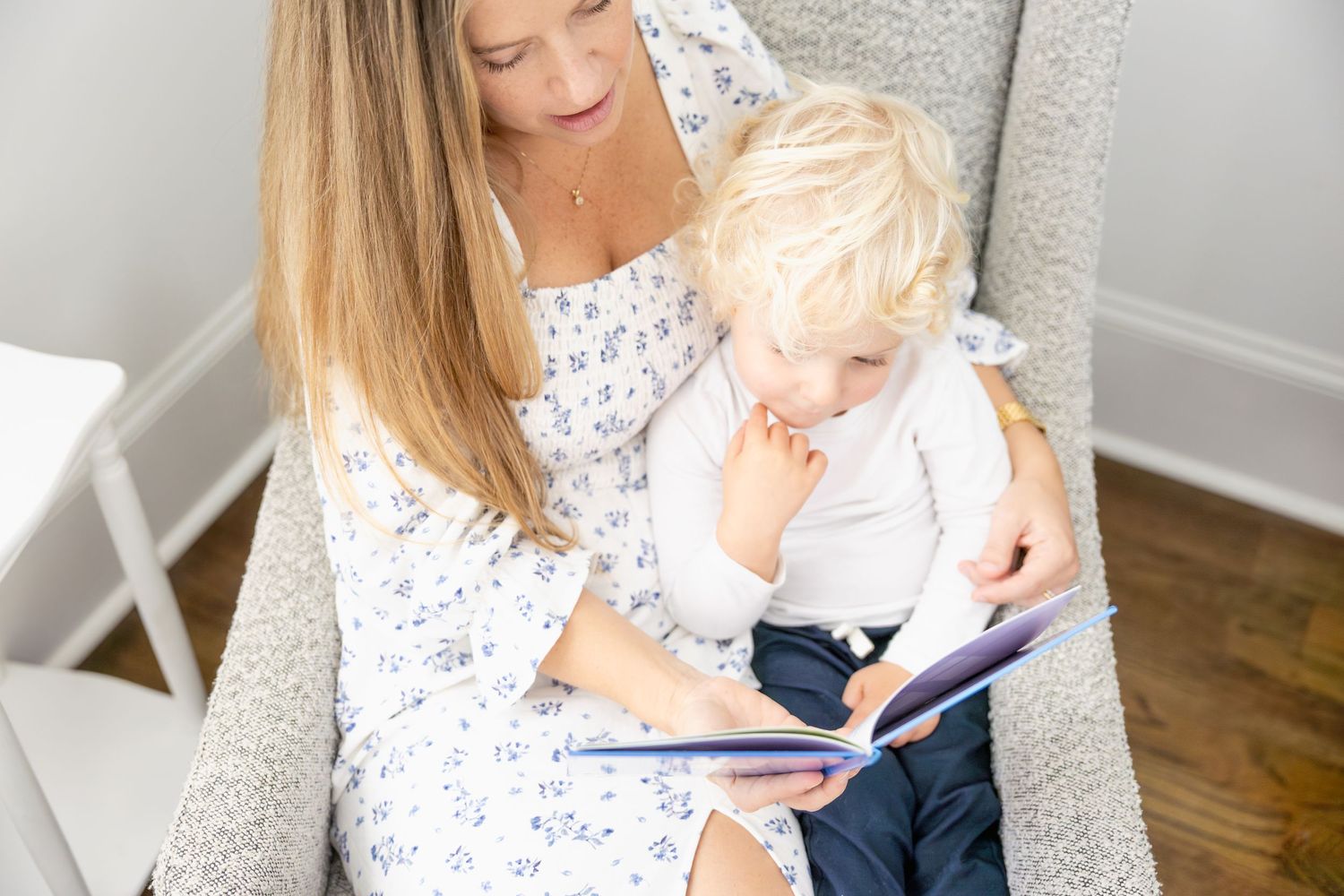 Reading together in a cozy gray armchair wearing matching floral dresses.