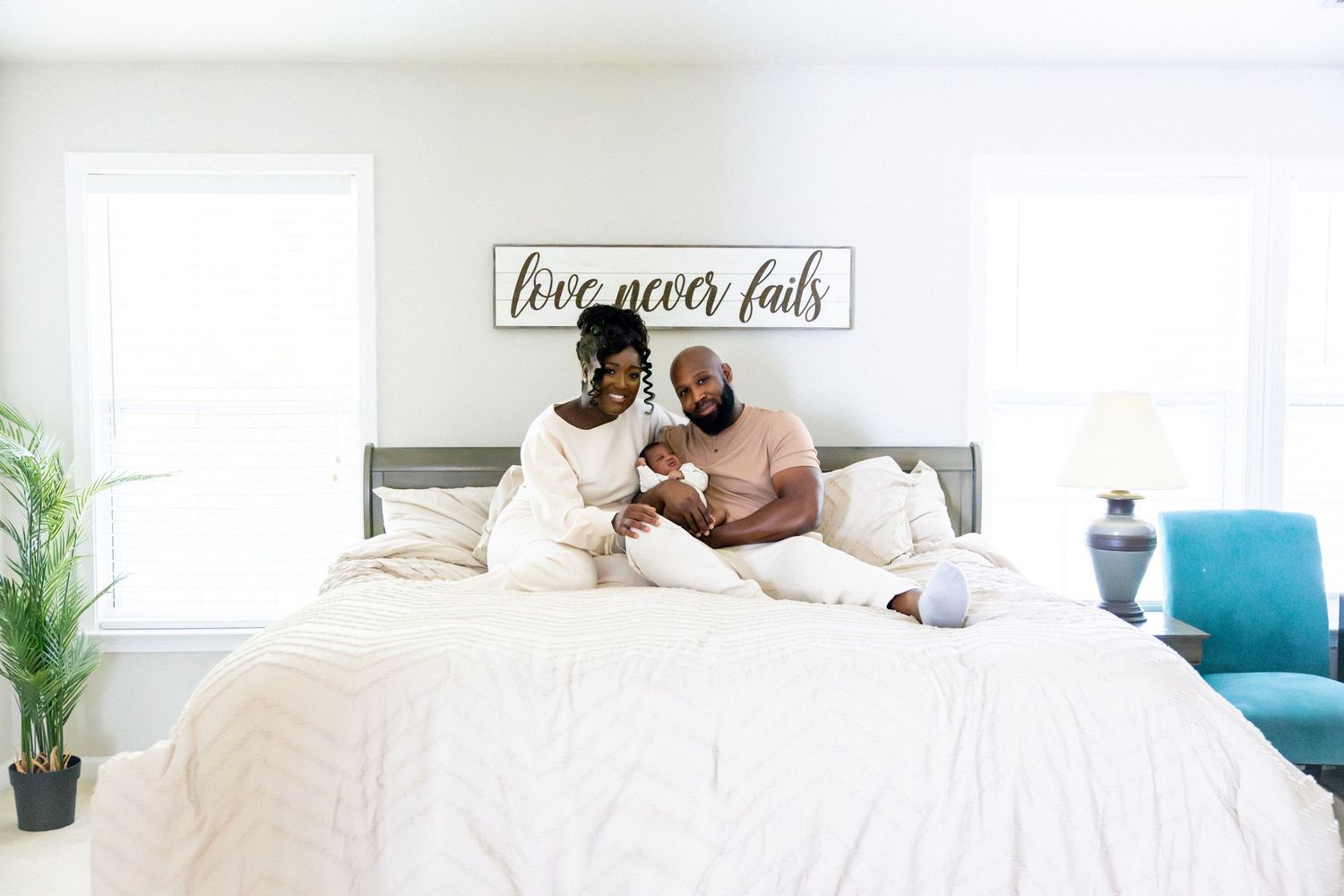 Bright white bedroom interior with turquoise accents and 'love never fails' wall art.