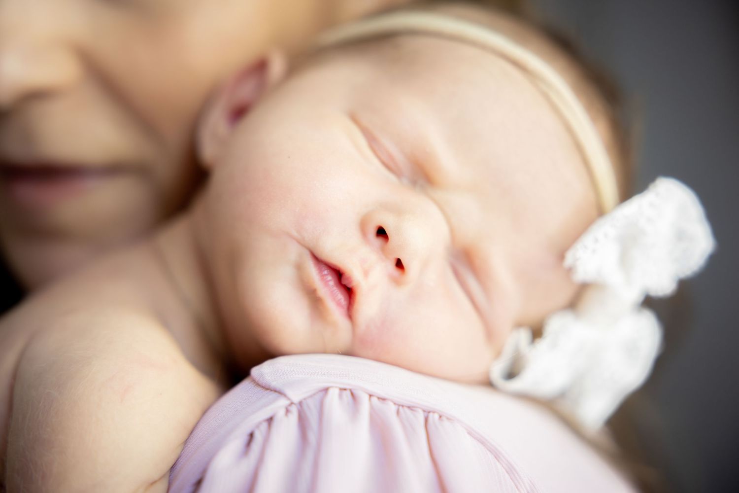 Sleeping baby in soft pink attire against dark background with dramatic lighting.