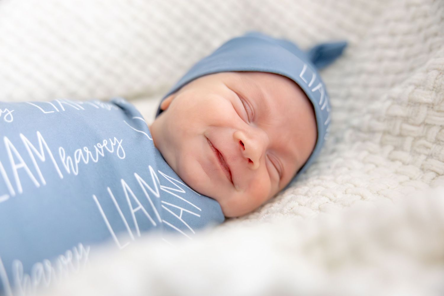 A sleeping infant rests peacefully on white bedding with blue accents.