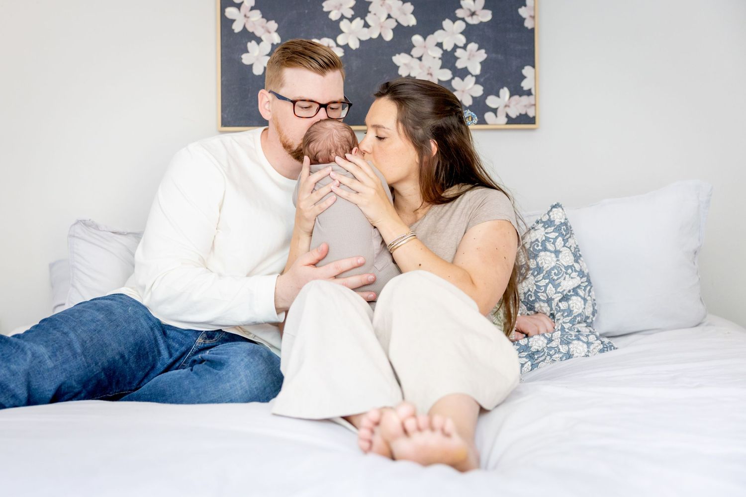 A couple shares a tender moment while relaxing together on a bed with white linens and floral wall art.
