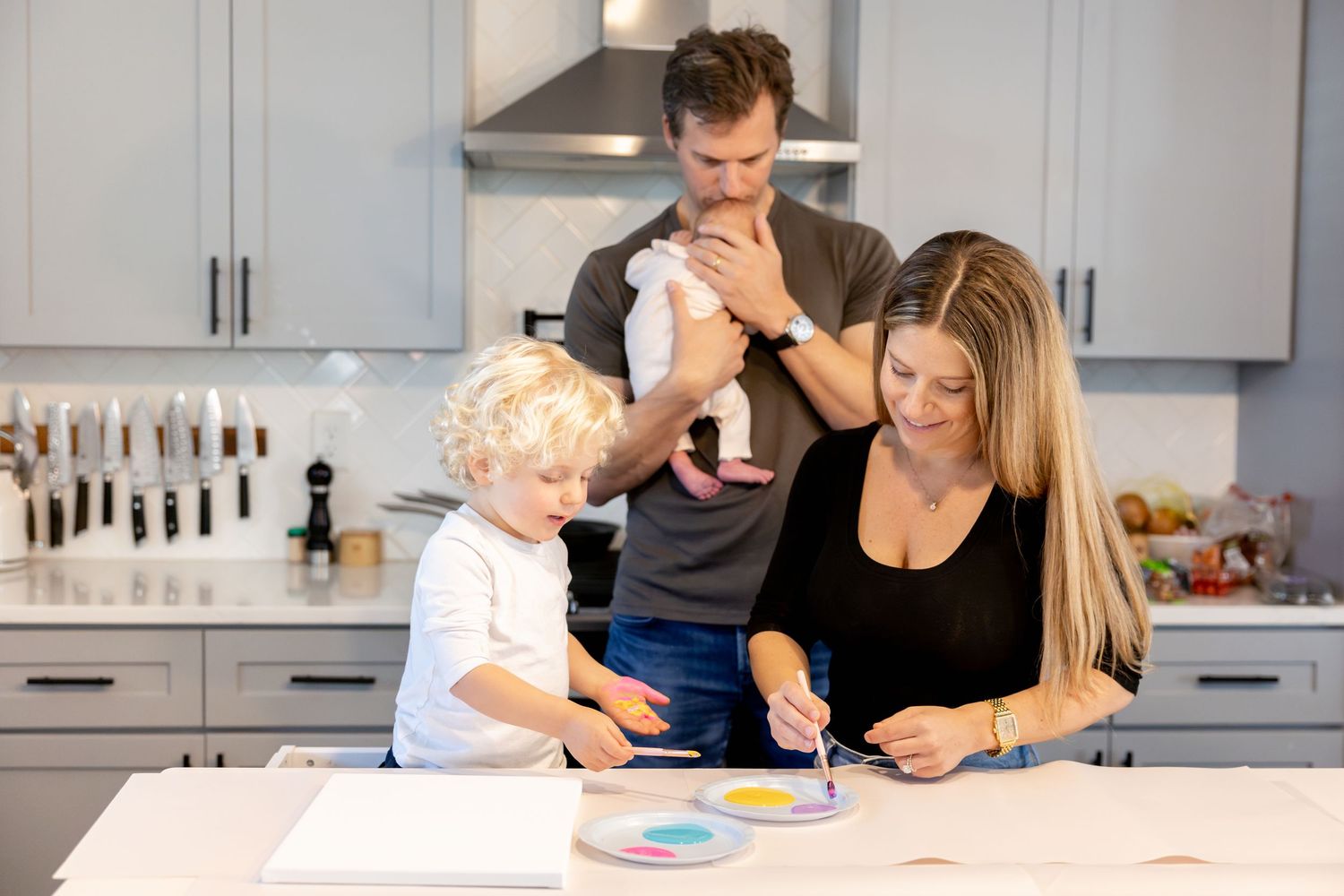 Family cooking together at white marble kitchen counter with colorful ingredients.