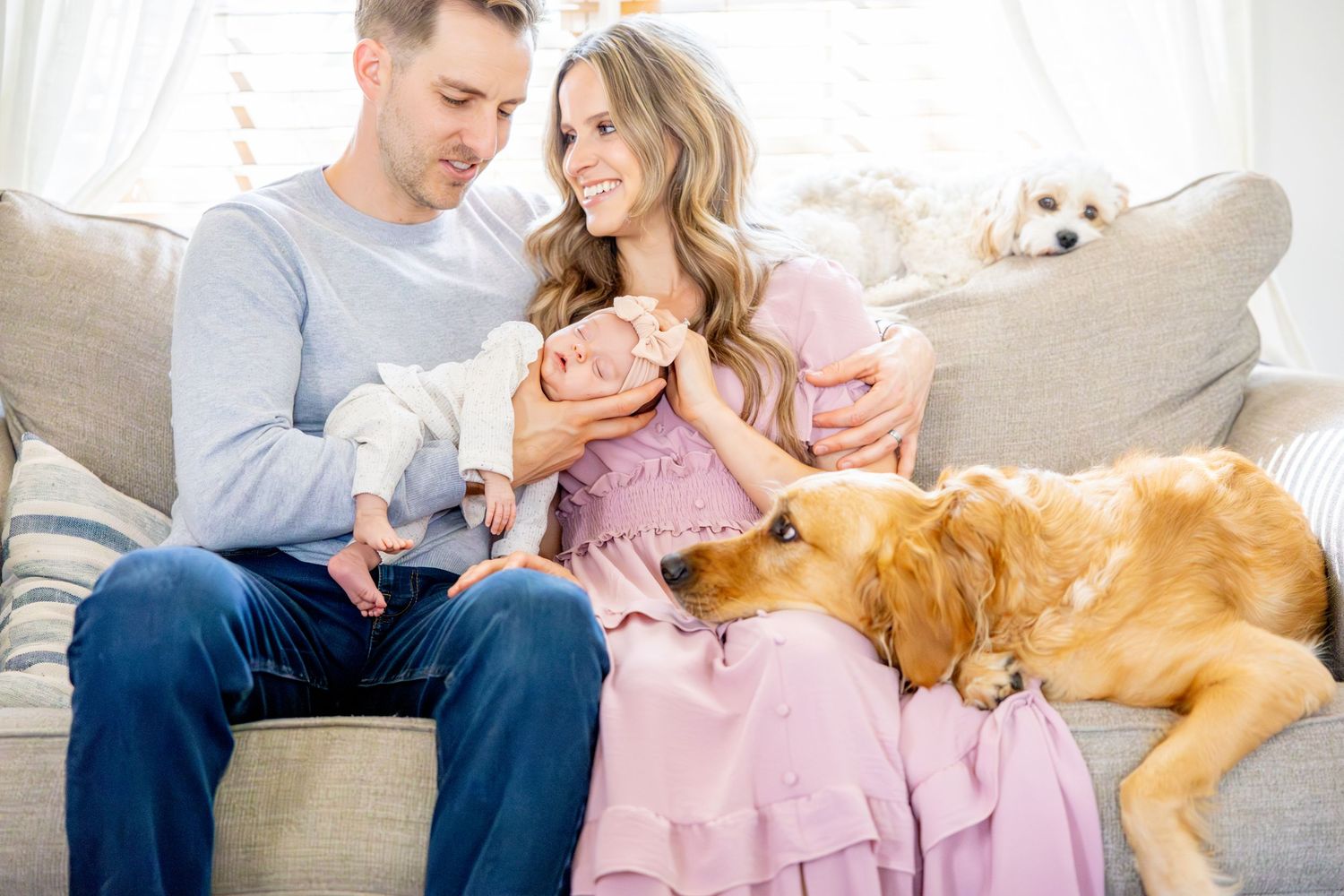 Couple on sofa with two dogs sharing intimate moment while holding their newborn baby.