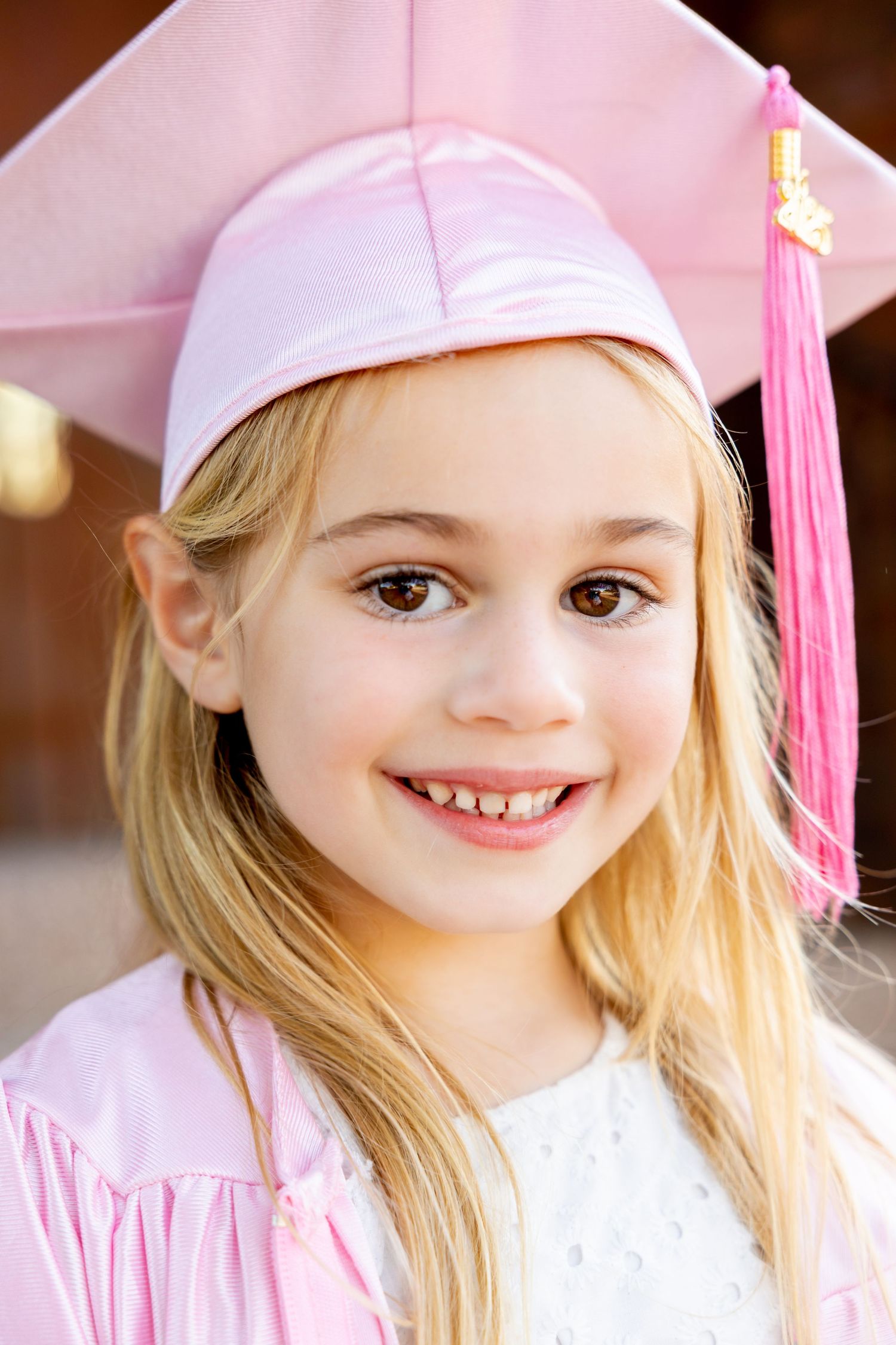 Close-up sequence of child in pink kindergarten graduation cap with tassel smiling at camera.