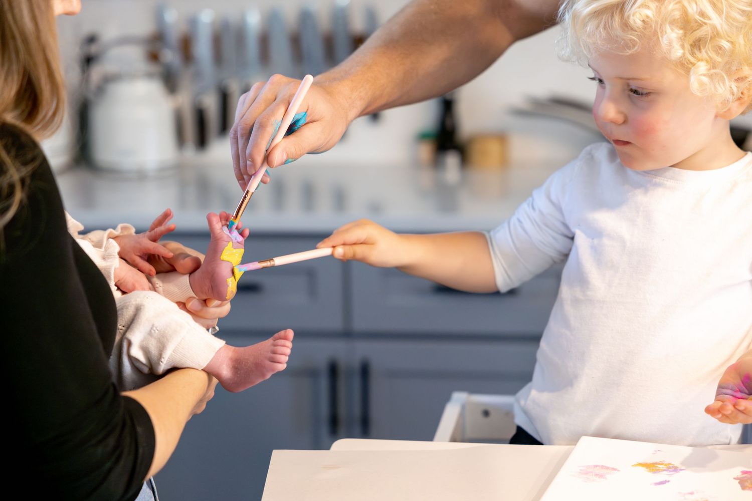 Small child using fingerpaint to create colorful artwork on paper while being assisted by an adult.