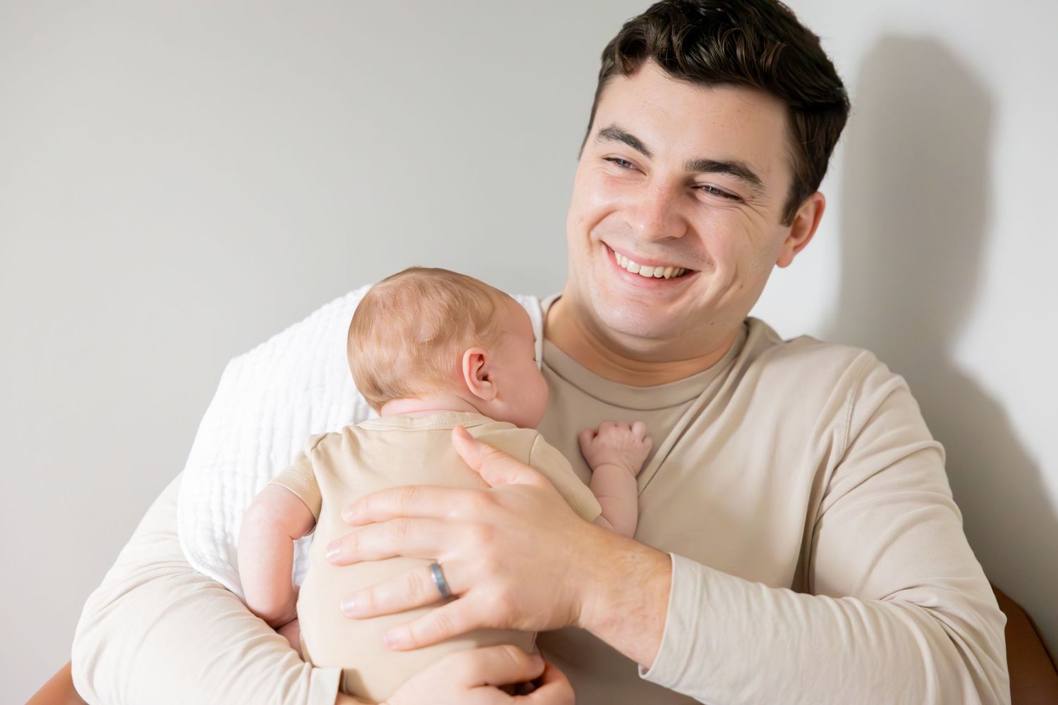 Parent wearing cream sweater holds and smiles at baby in candid home portrait.
