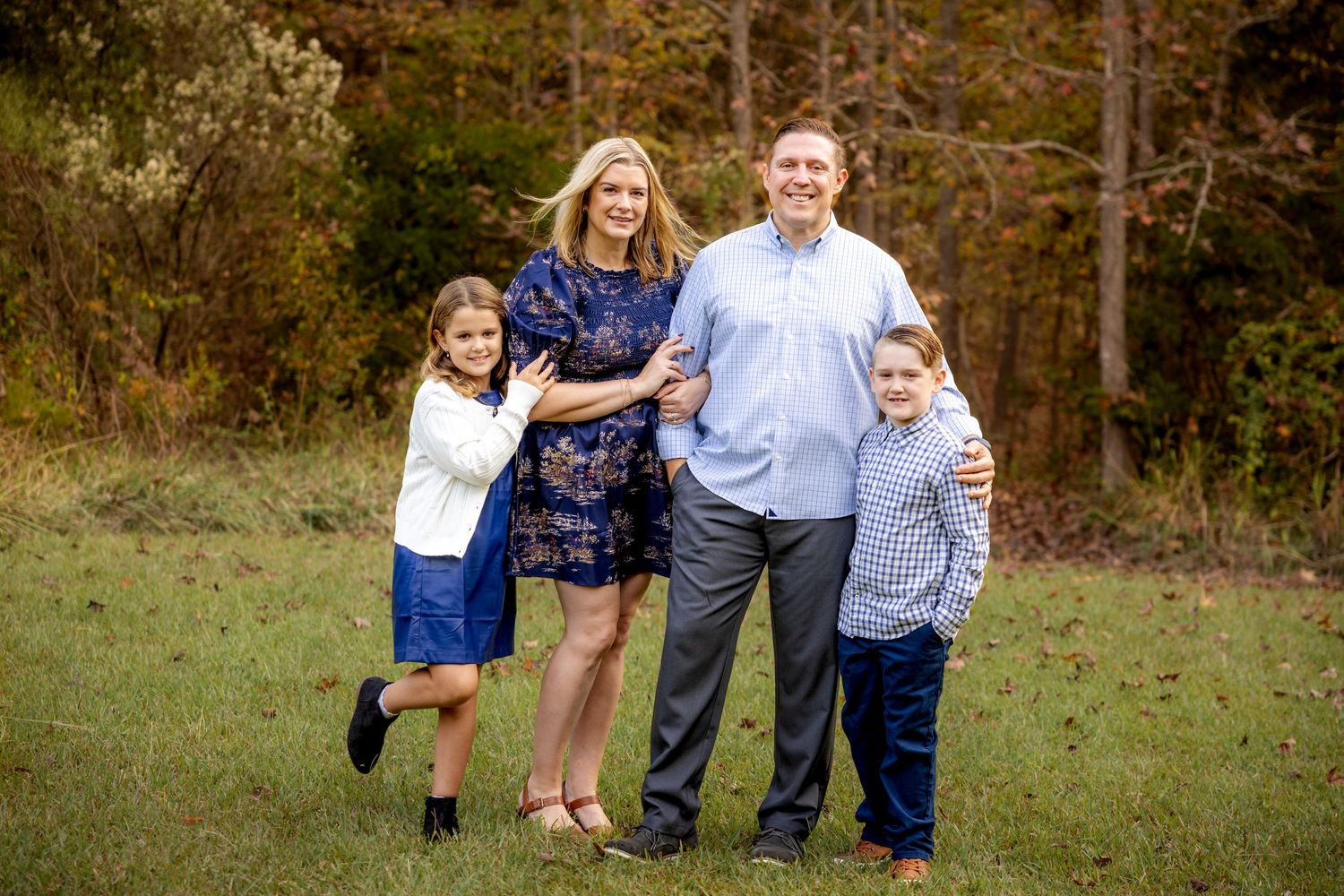 Family poses together in a grassy field during golden hour sunset.