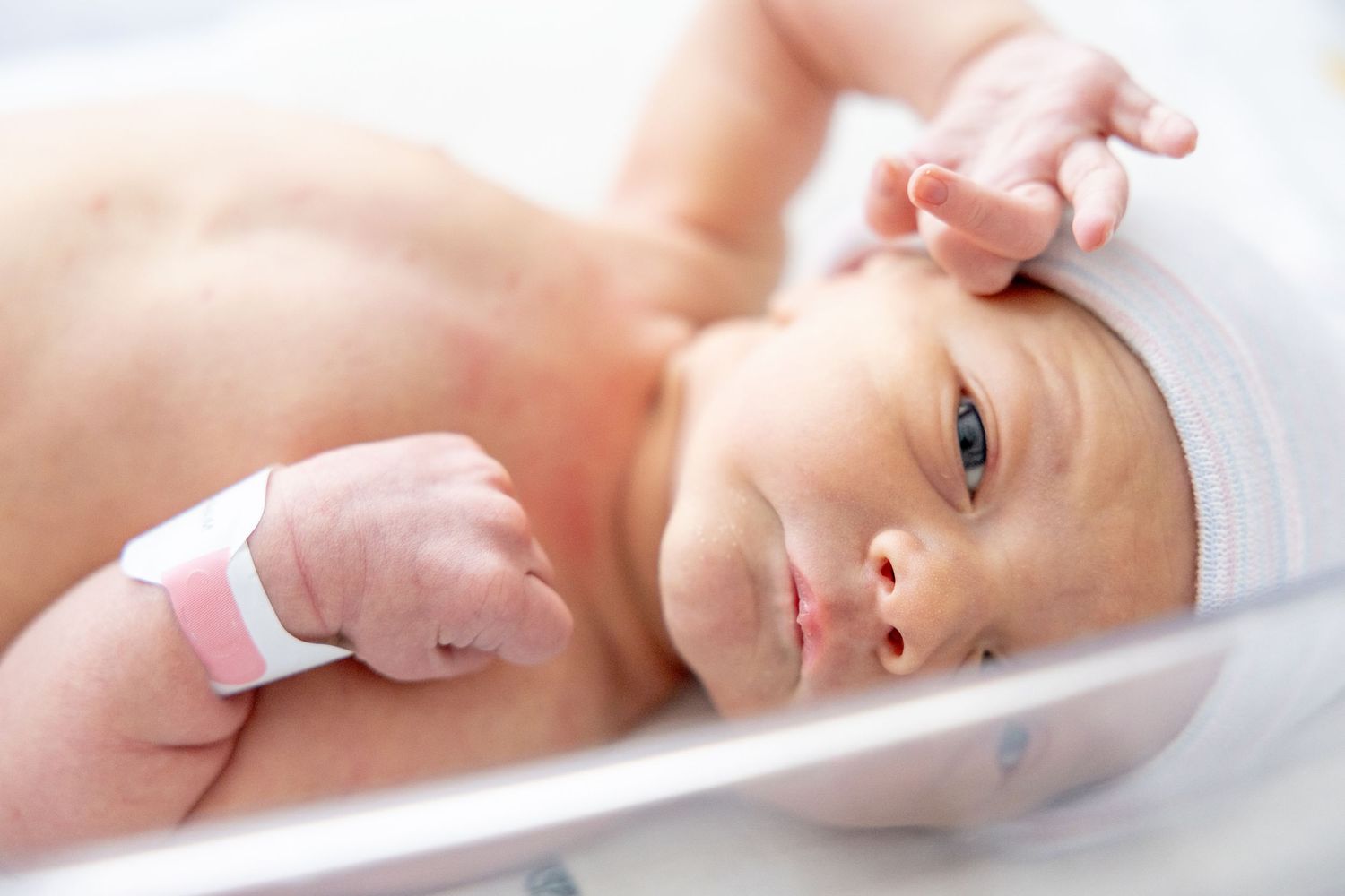 Newborn baby wearing white cap lying on medical examination table.