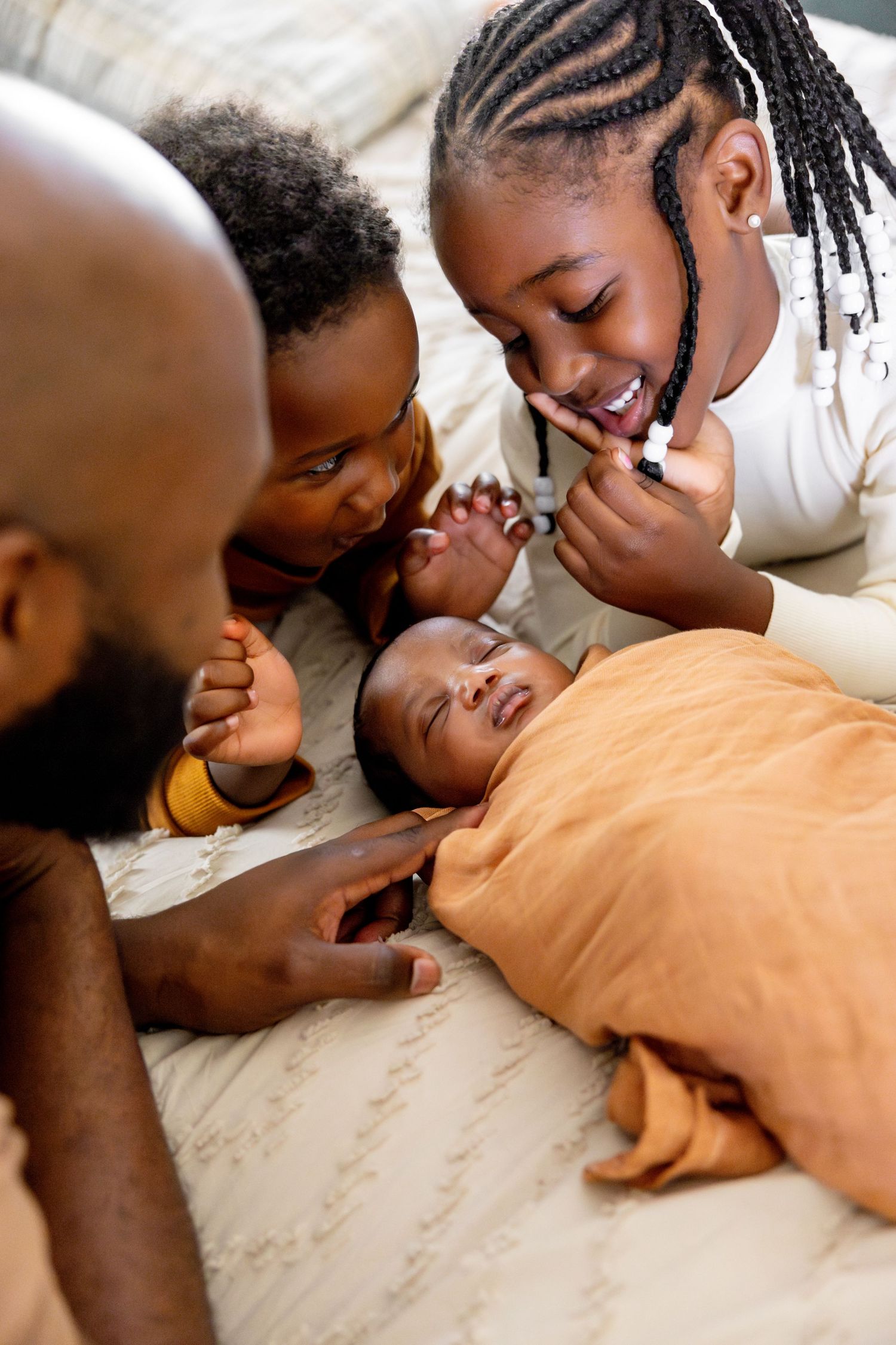 Family gathering close together on bed sharing laughs with sleeping baby.