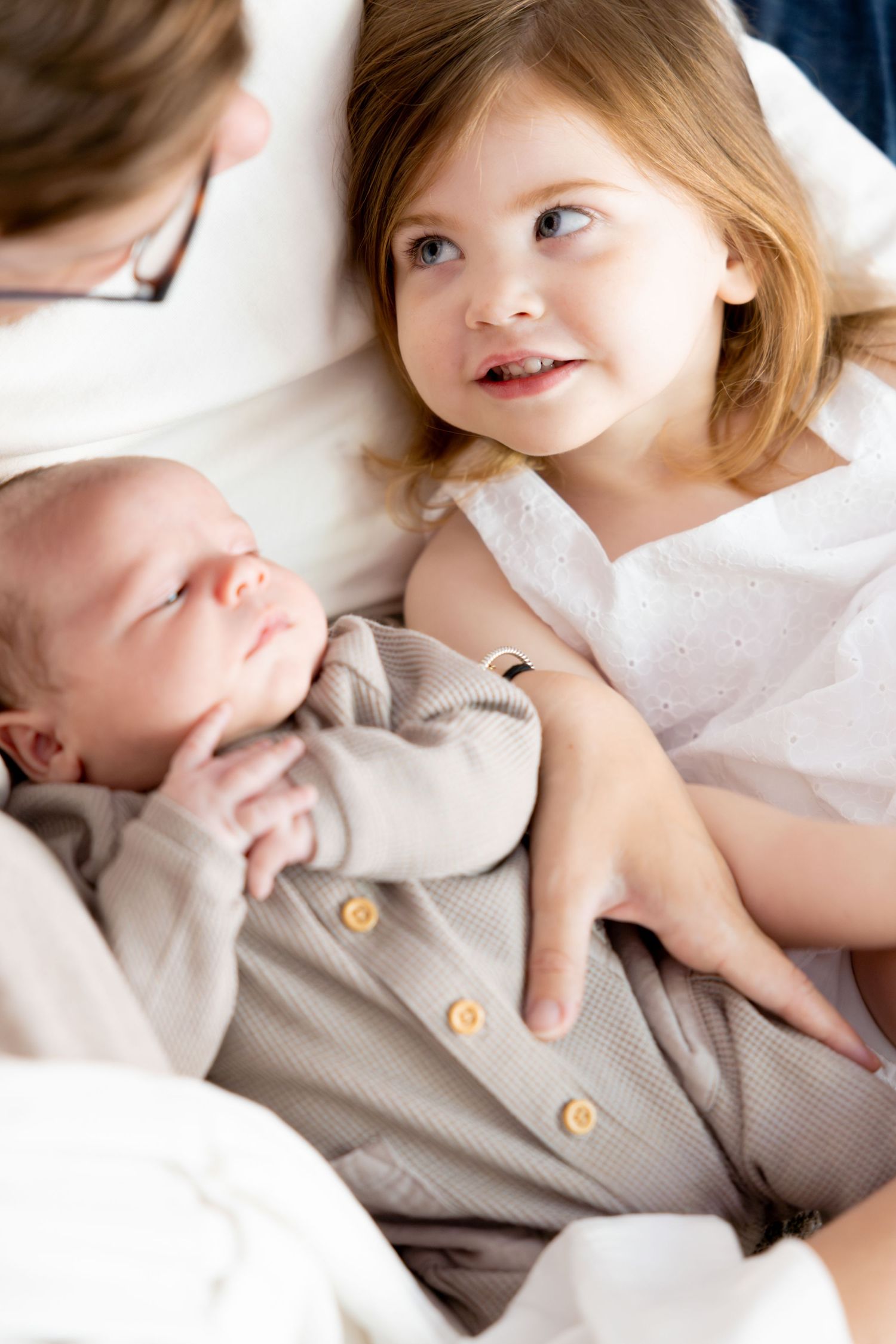 Siblings share tender moment as older child gazes at baby in gray outfit.
