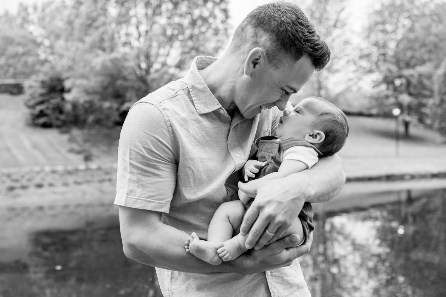Tender black and white portrait by a reflective pond in a park setting.