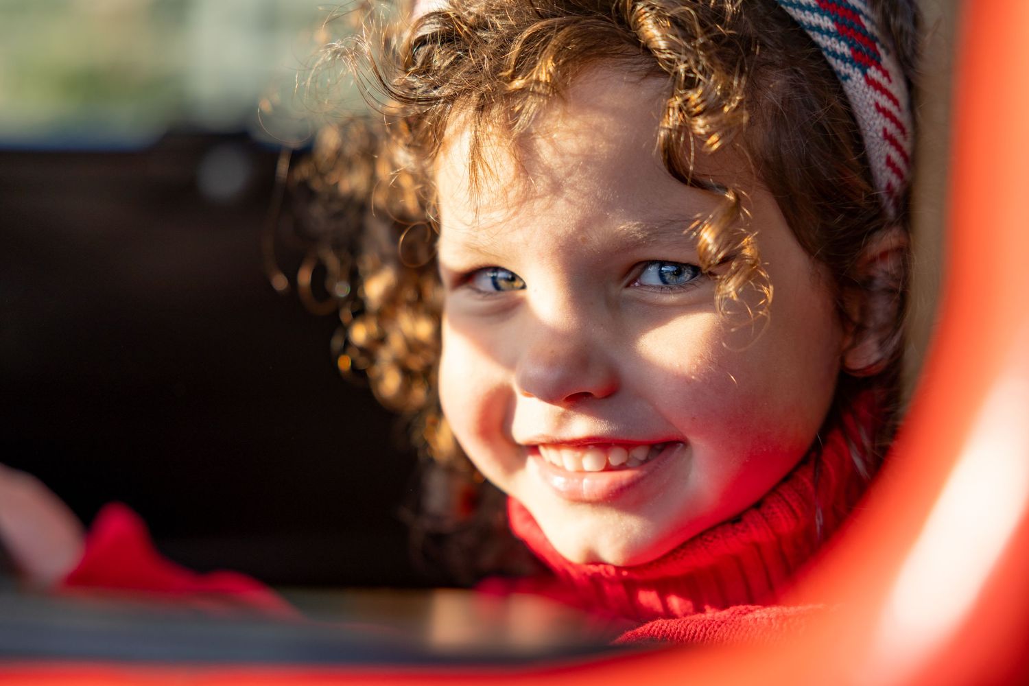 View through a car window showing girl wearing a red and white striped headband.